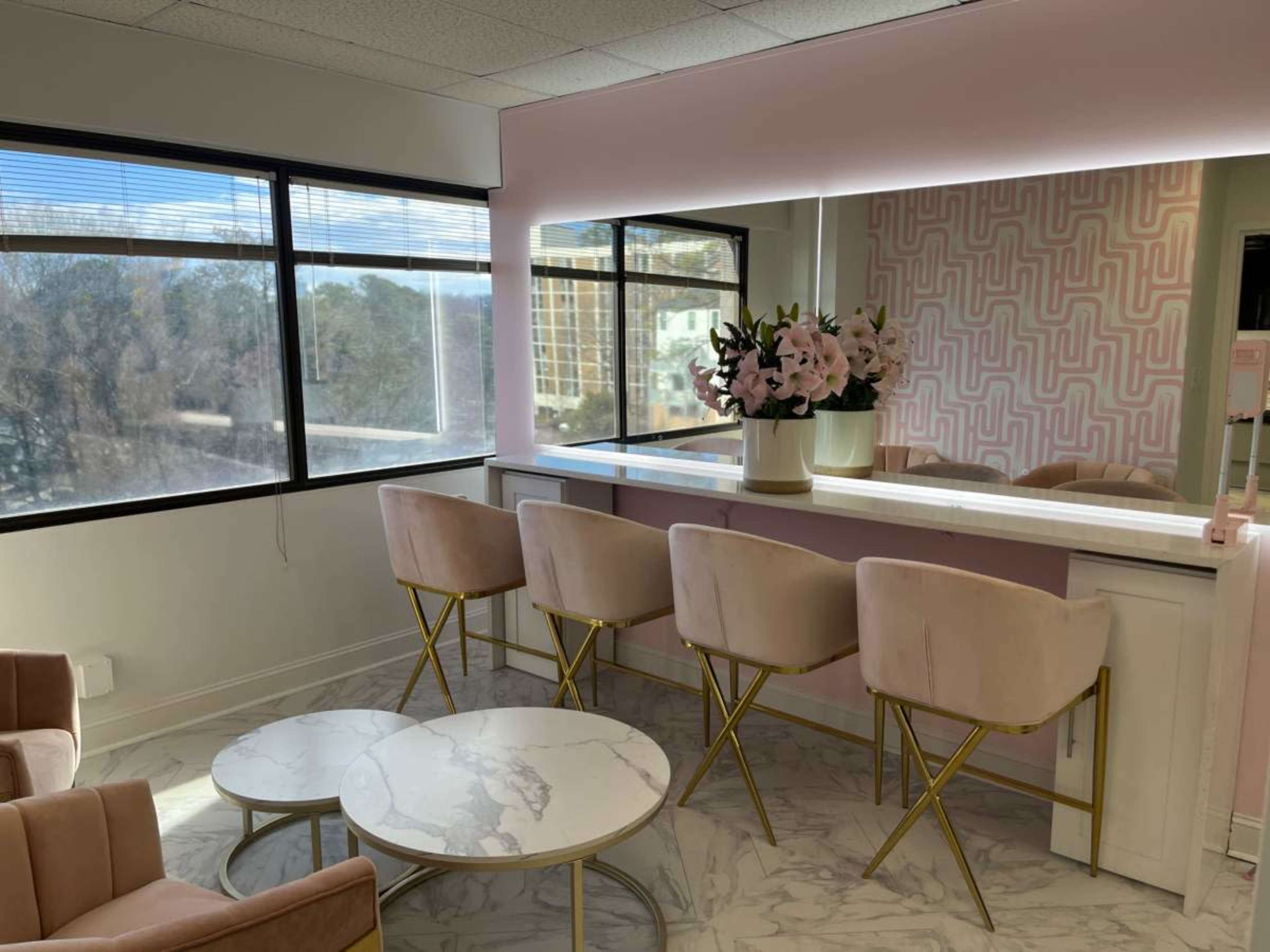 A modern lounge area features a marble table, pink velvet chairs, and large windows overlooking a cityscape.