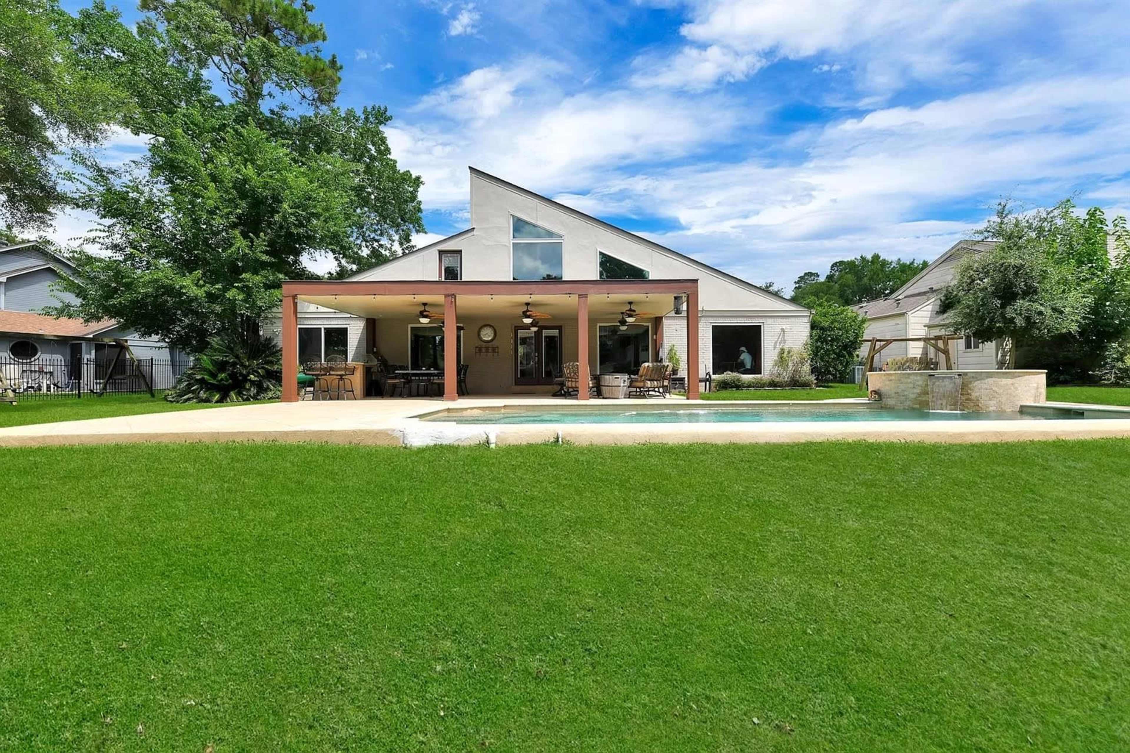 A modern house with a slanted roof features a covered patio and swimming pool in a grassy yard.