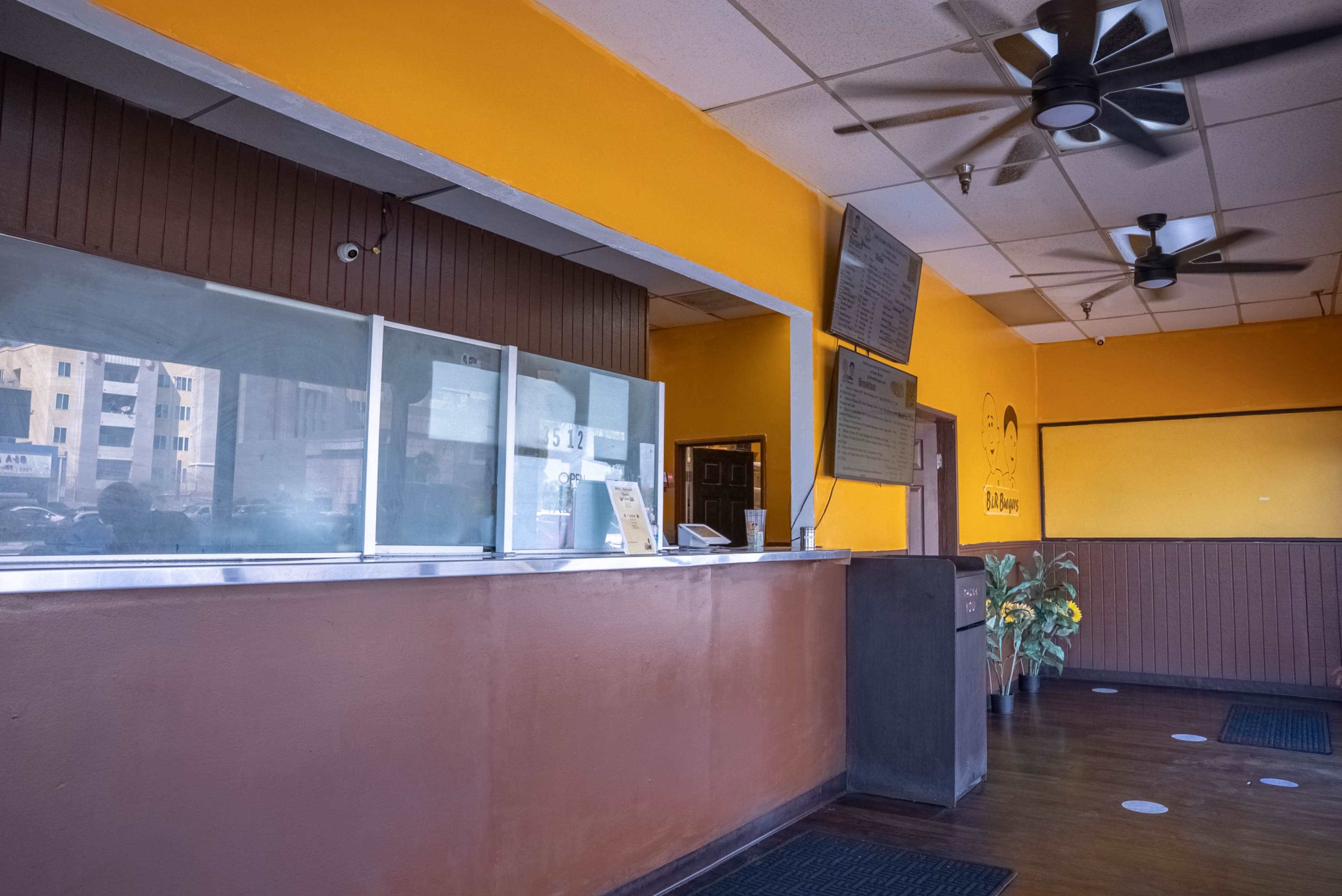 The image shows an empty restaurant interior featuring a service counter, gray walls, and an orange accent wall.