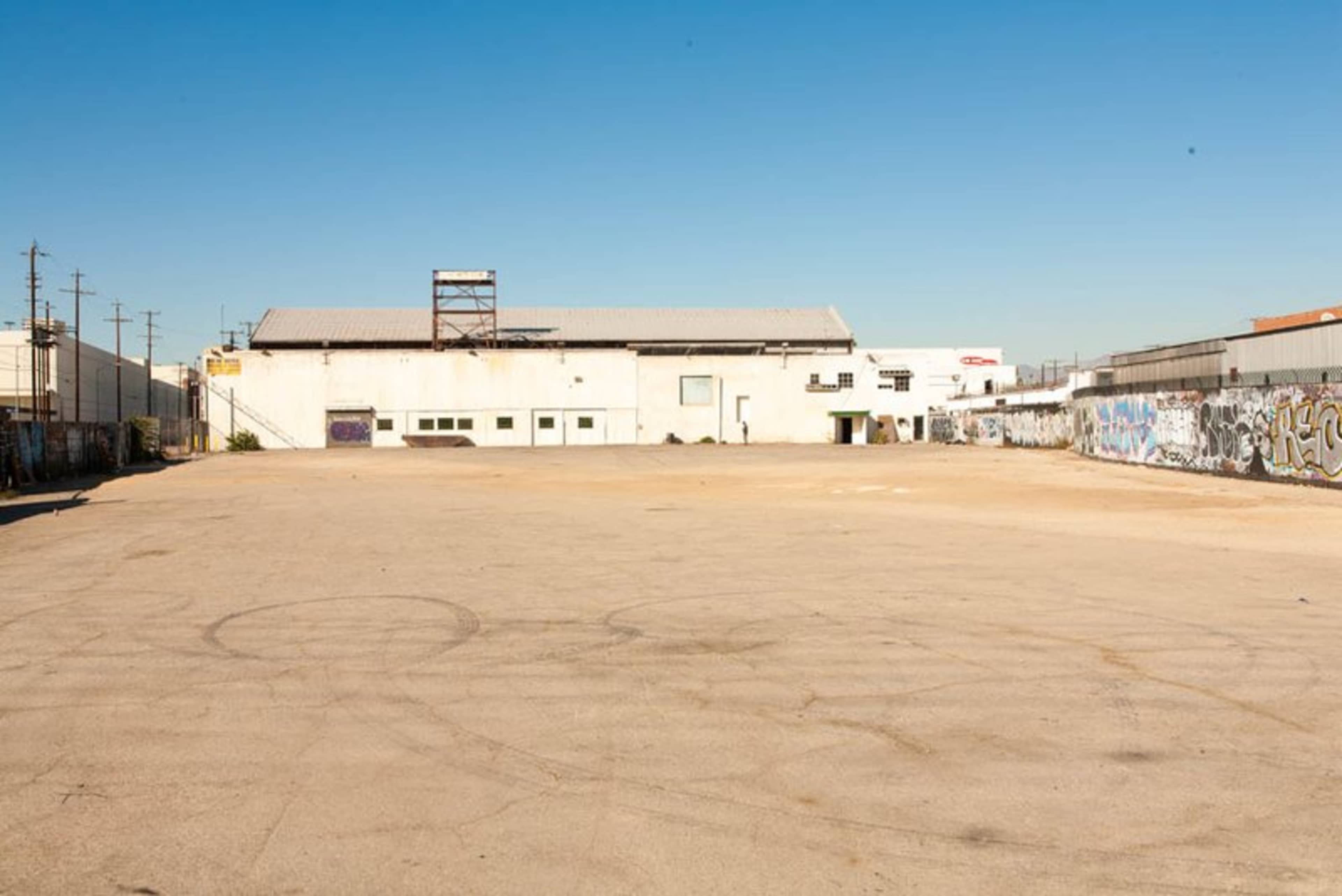A large, empty lot with a concrete surface and a single building covered in graffiti along its perimeter.