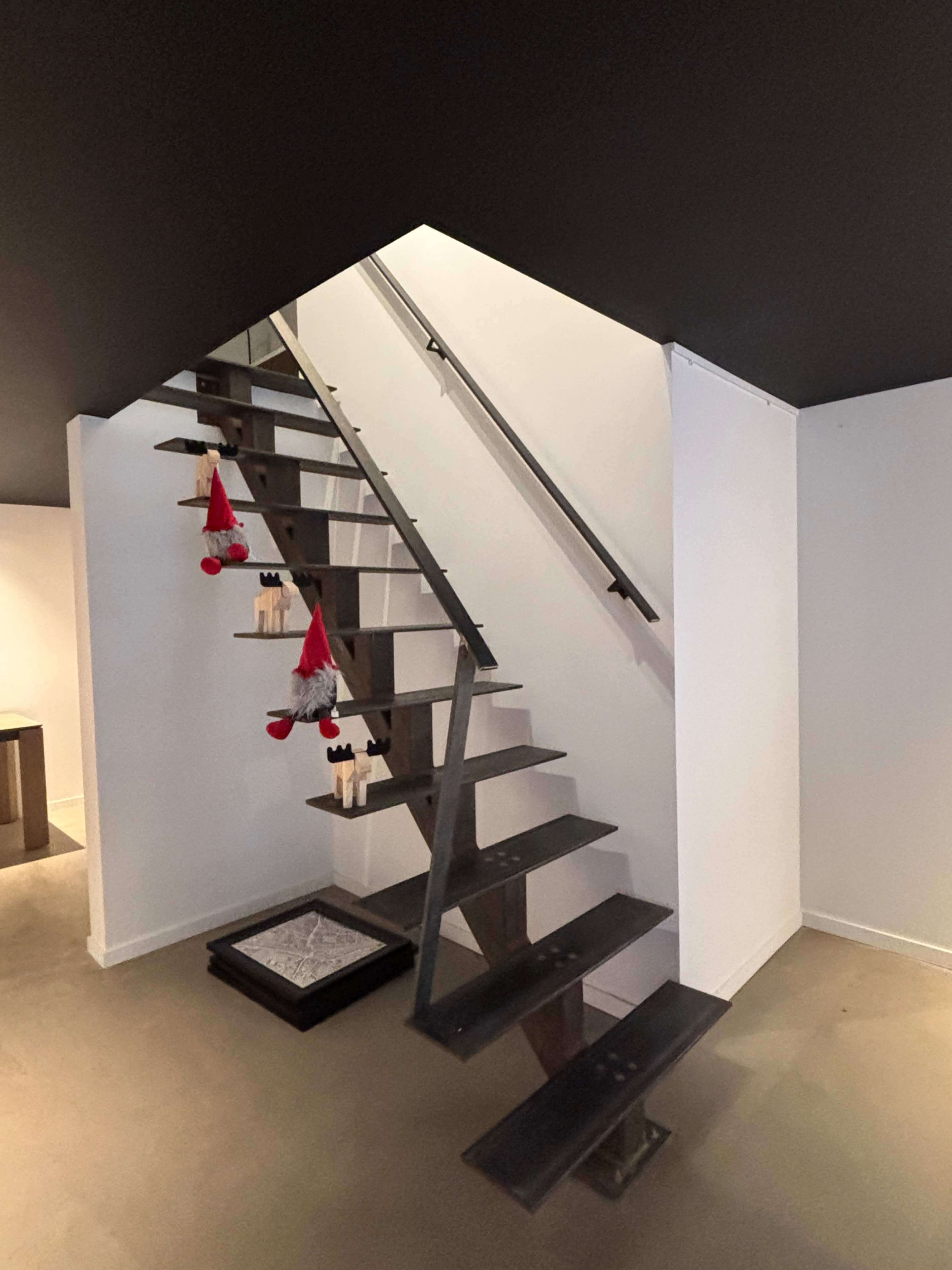 A modern staircase with metal steps leads to a second level, and holiday decorations are hung on the railing.