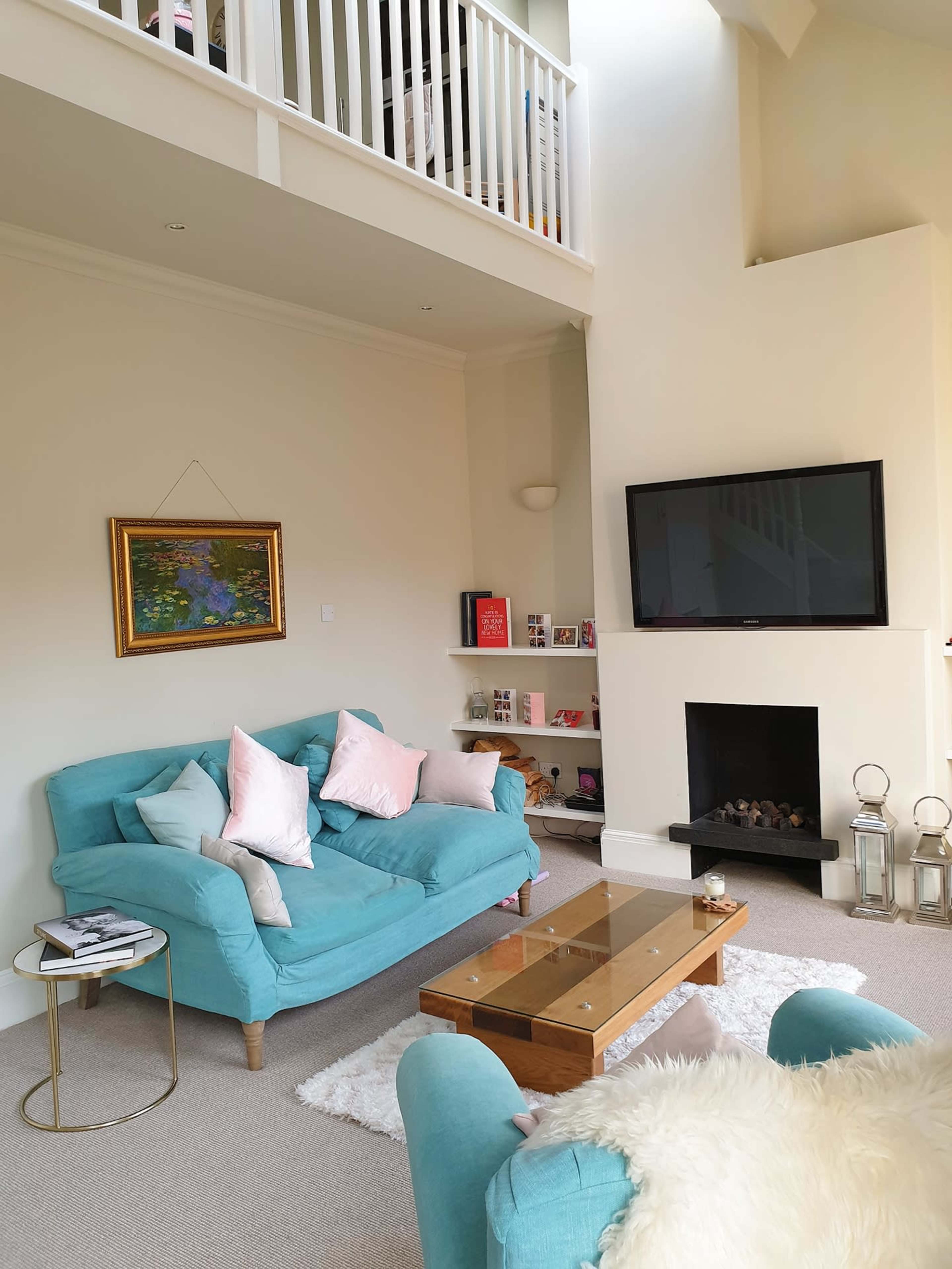 The image displays a cozy living room featuring a turquoise sofa, a wooden coffee table, a wall-mounted television, and a fireplace with decorative lanterns.