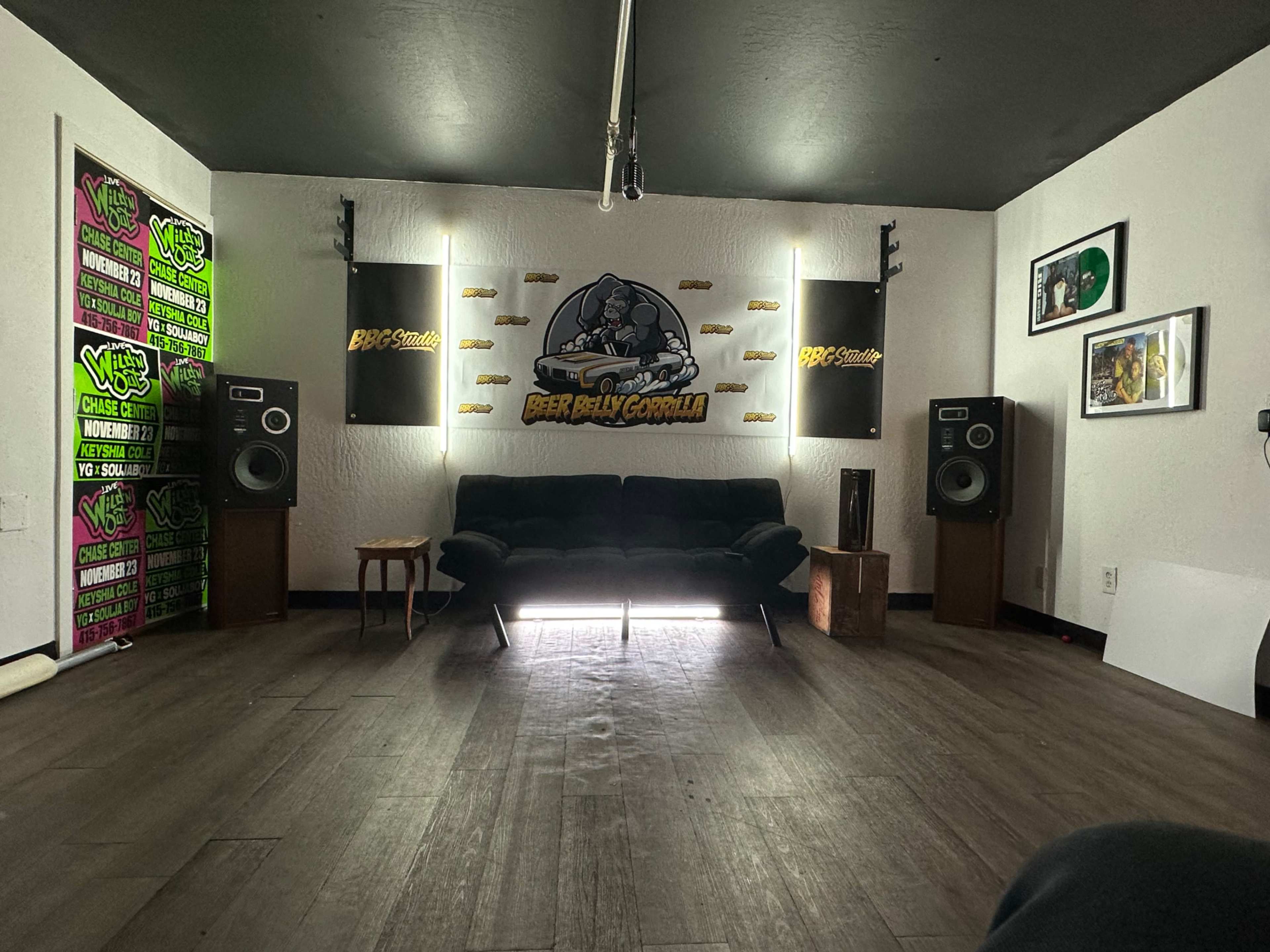 The image shows a music studio with a black couch, large speakers, and various decorations on the walls.