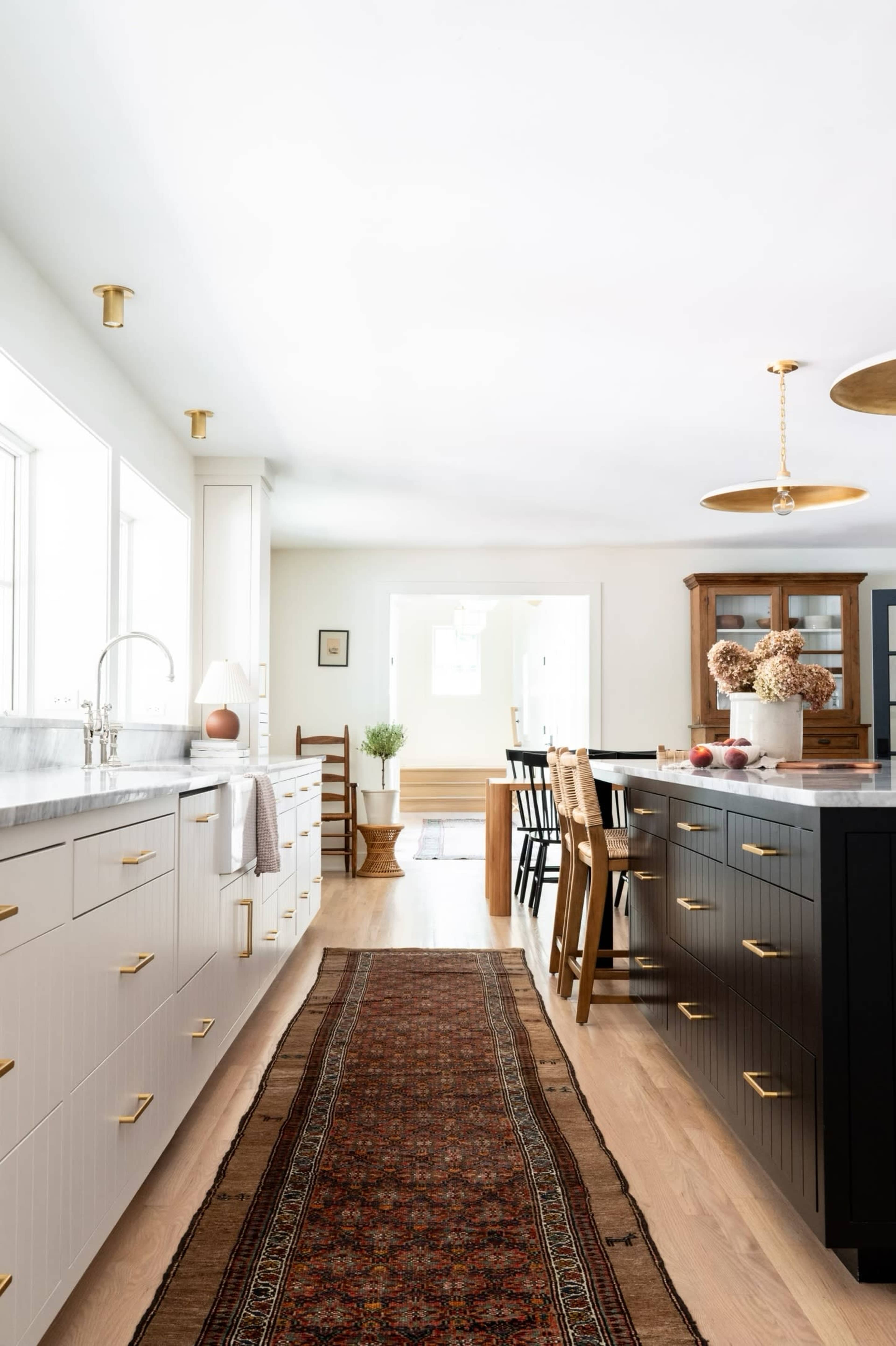 A spacious kitchen features a central runner rug, contrasting black and white cabinets, and pendant lighting above a dining area.