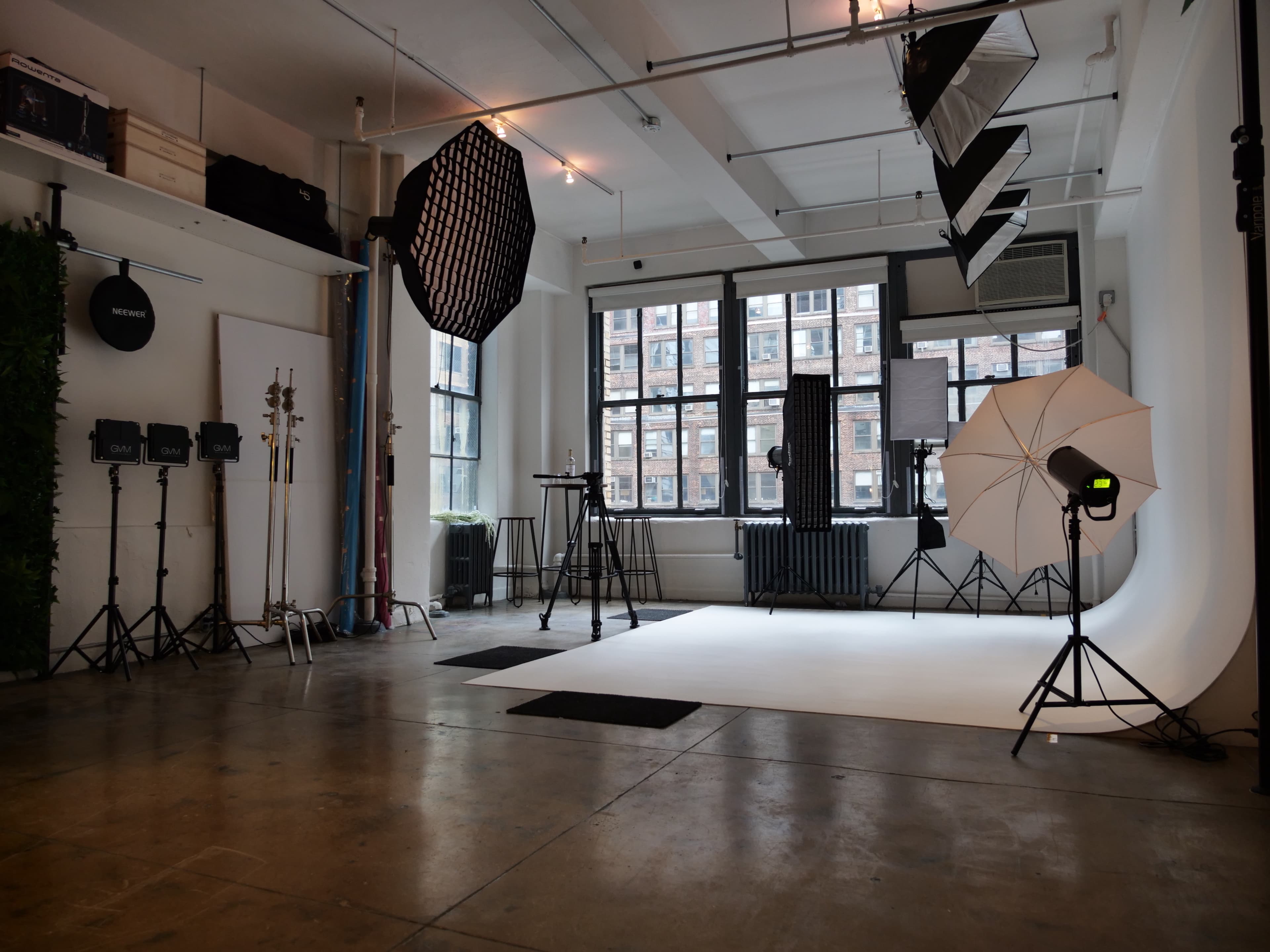 A spacious photography studio with various lighting equipment and a plain backdrop set up for photo shoots.