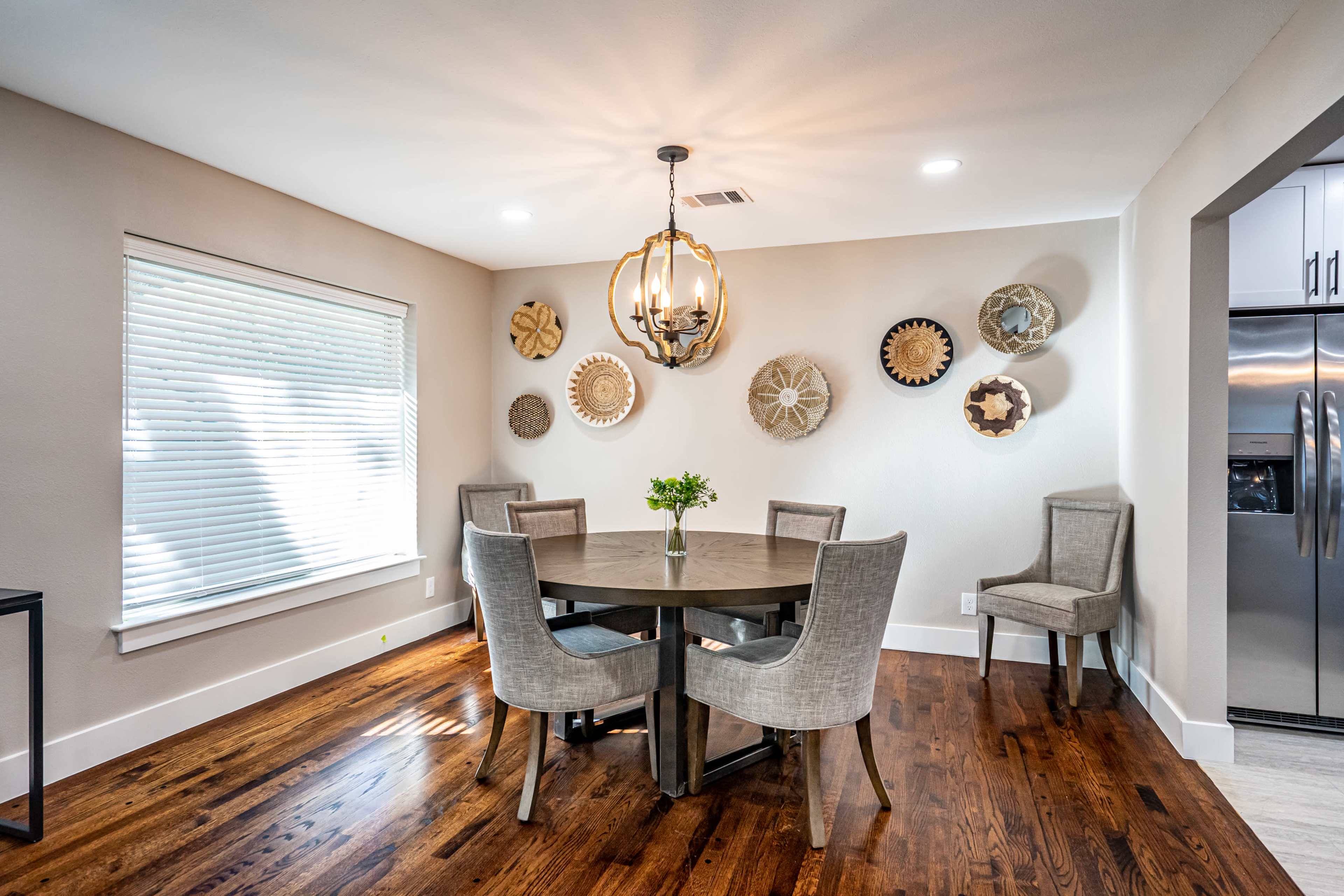 A modern dining area features a round table surrounded by four chairs, with decorative wall plates and a pendant light overhead.