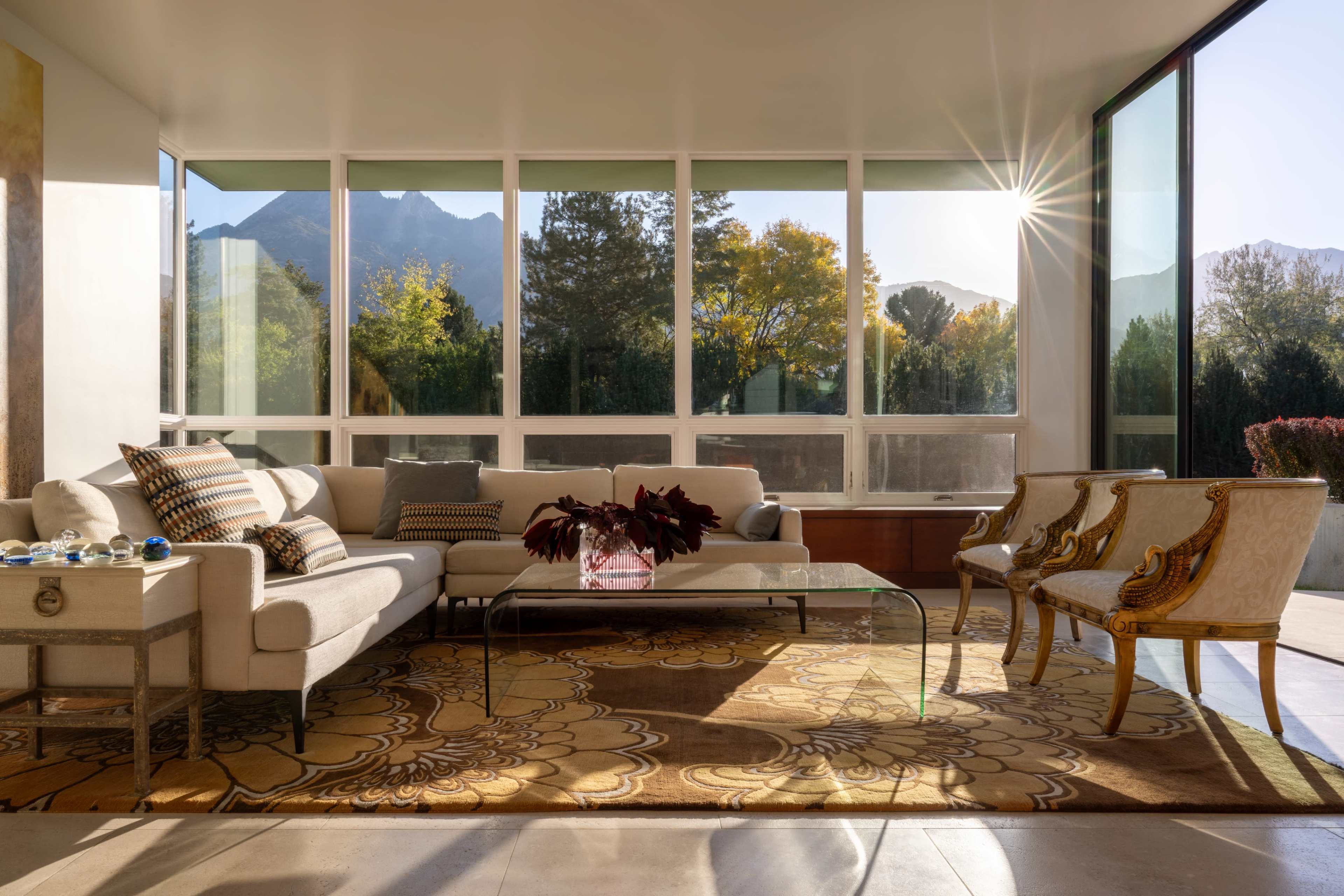 A bright and spacious living room features a modern couch, elegant chairs, and large windows that overlook a scenic outdoor view.
