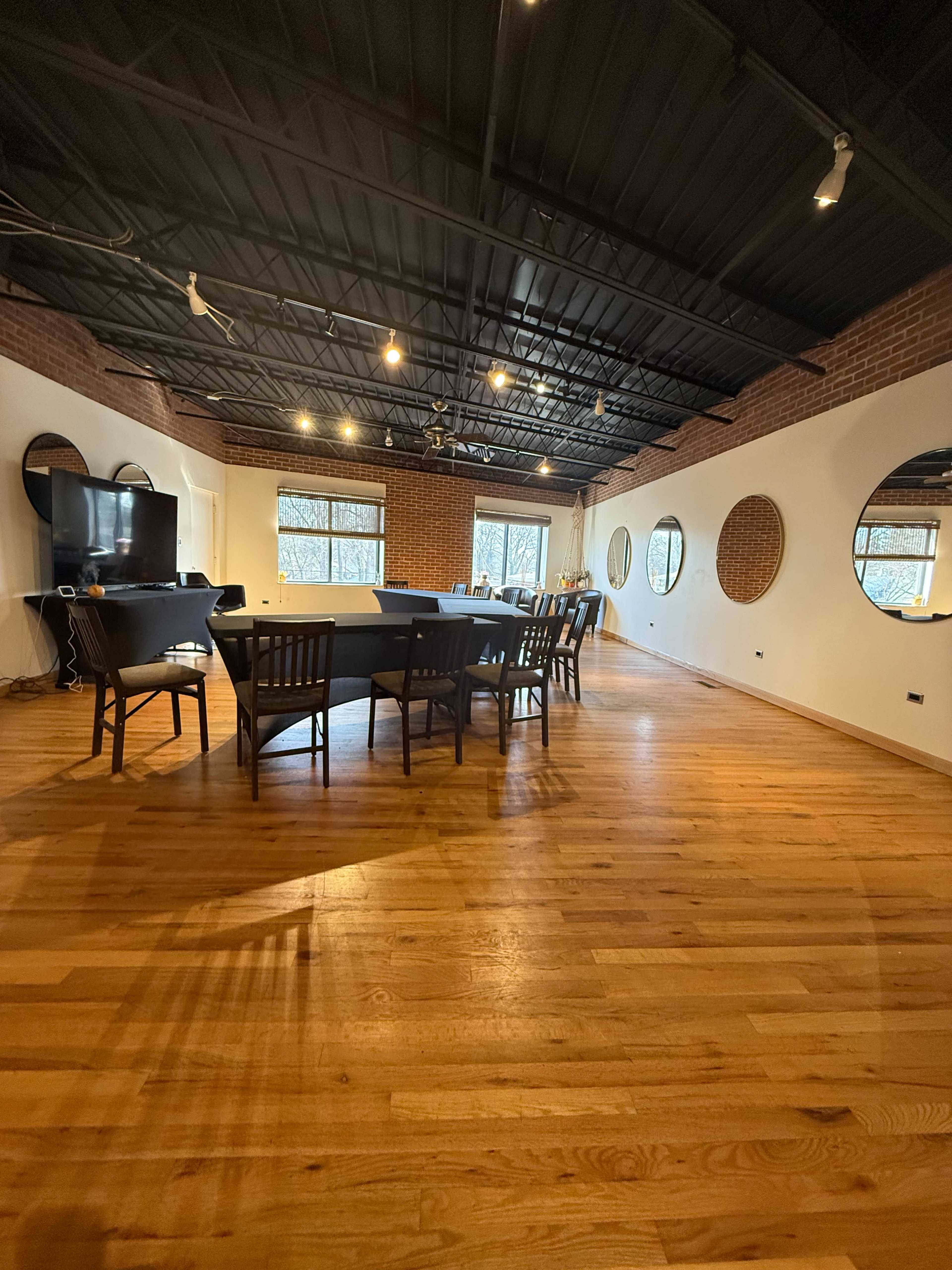 A large conference room features a rectangular table surrounded by wooden chairs, with large windows and circular mirrors on the walls.