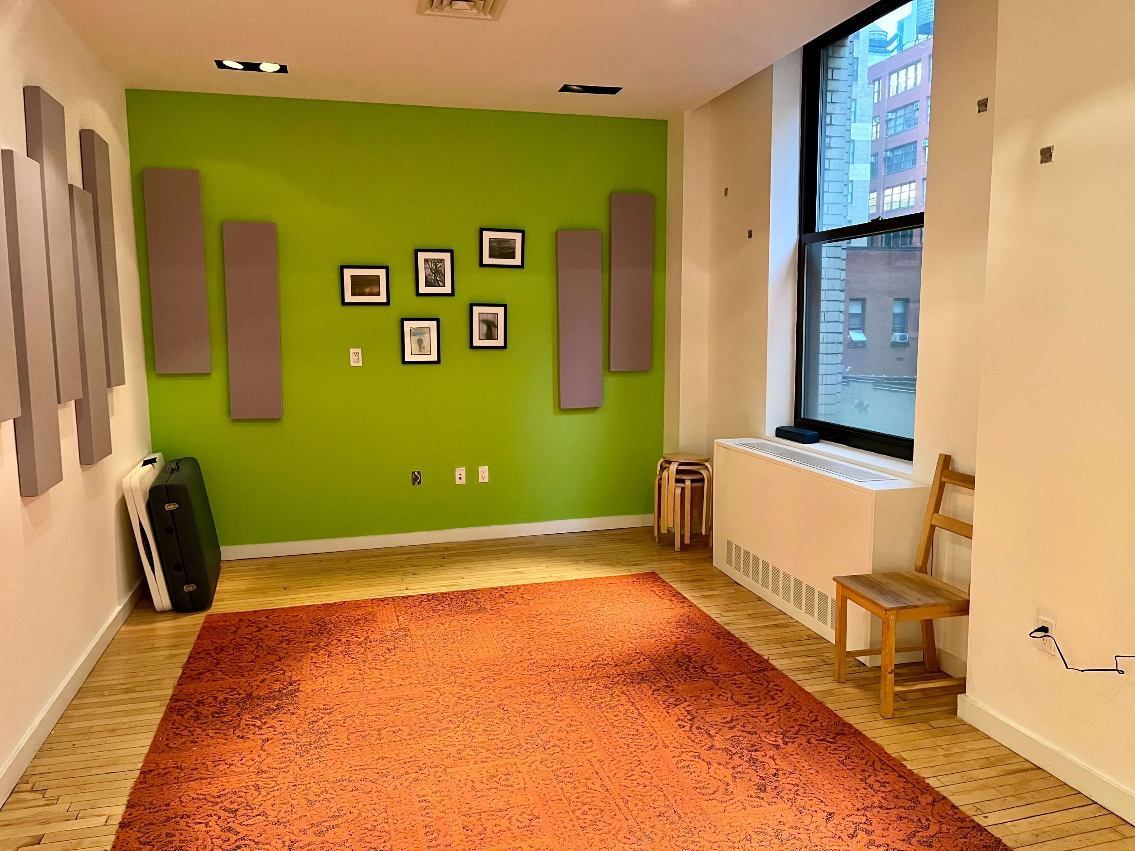 A room with a green accent wall, wooden flooring, a patterned rug, a single chair, and framed pictures on the wall.