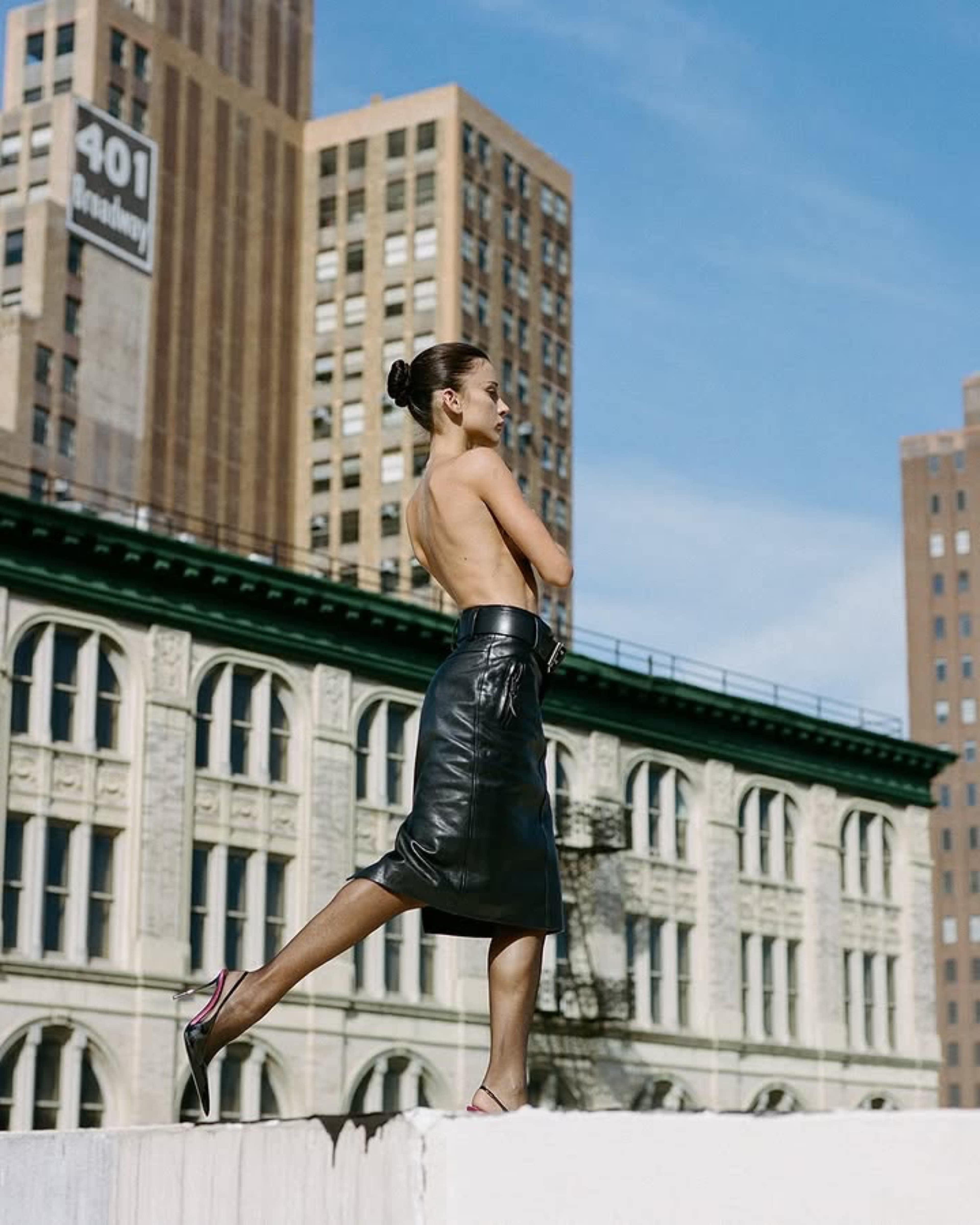 A woman poses confidently on a ledge with a city skyline in the background.