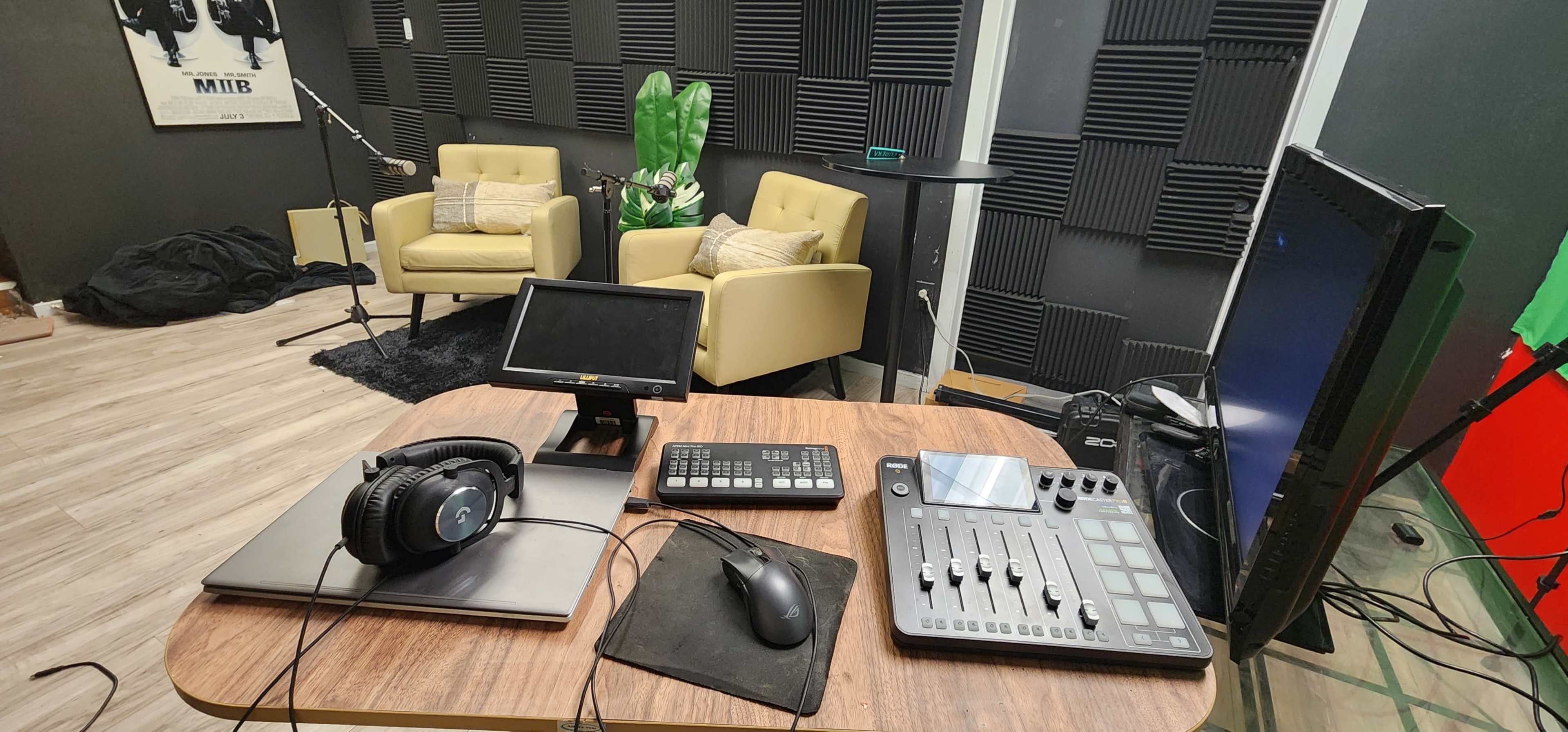 The image depicts a recording studio setup featuring a wooden desk with audio equipment, headphones, and two yellow chairs in a soundproofed room.