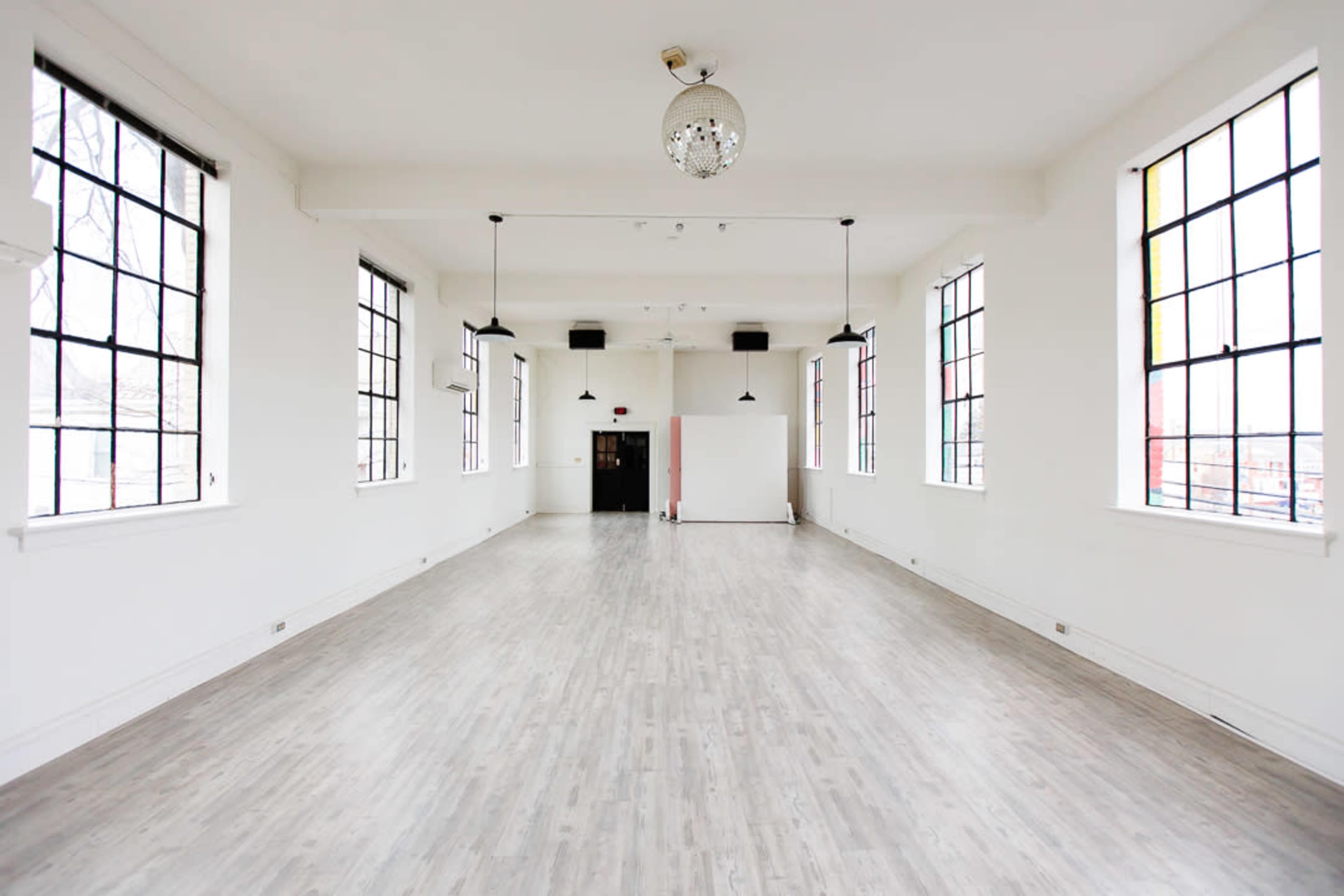 A spacious, empty room with large windows, wooden flooring, and a chandelier.