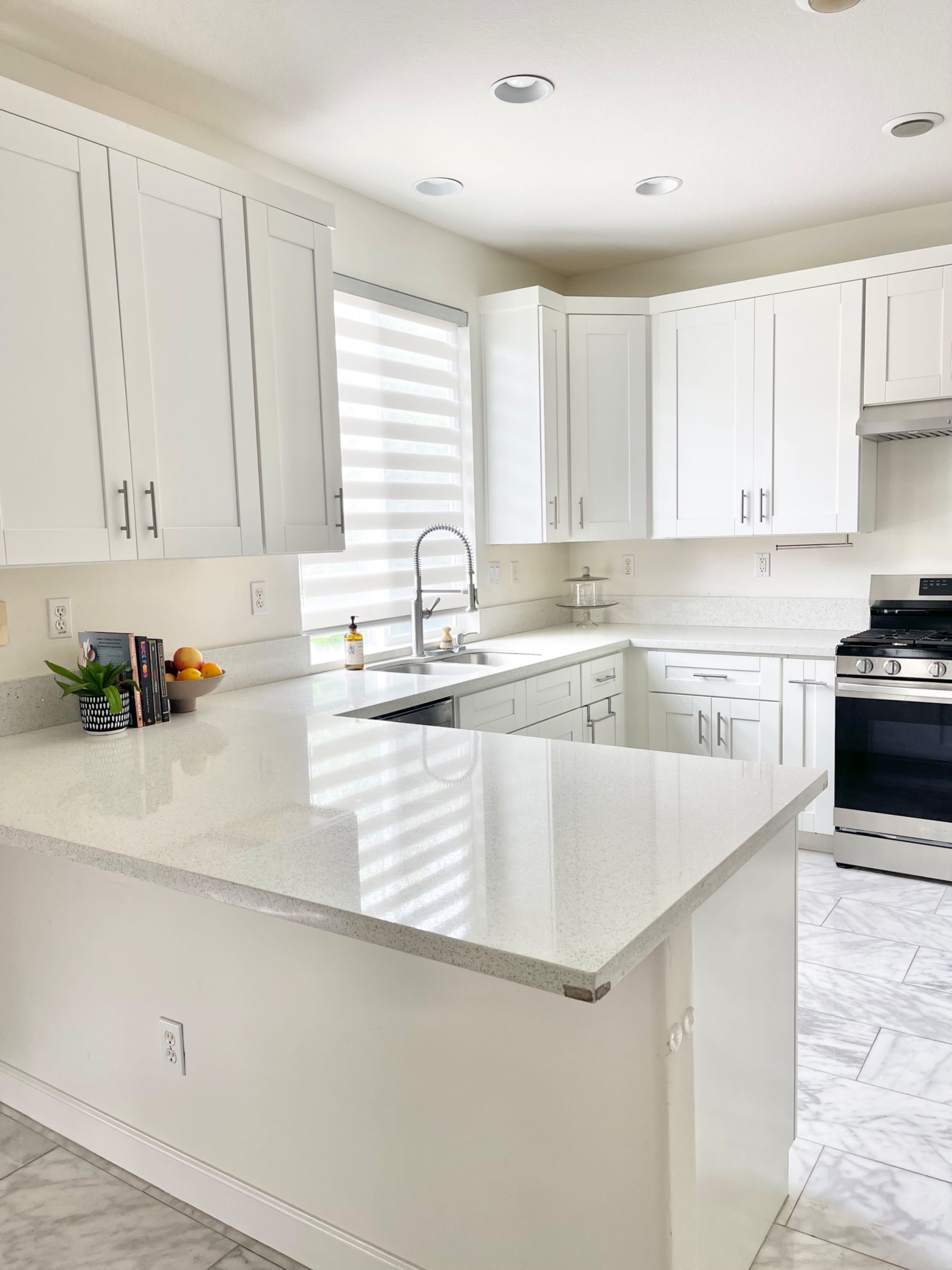 A modern kitchen features white cabinets, a large island with a quartz countertop, and stainless steel appliances.