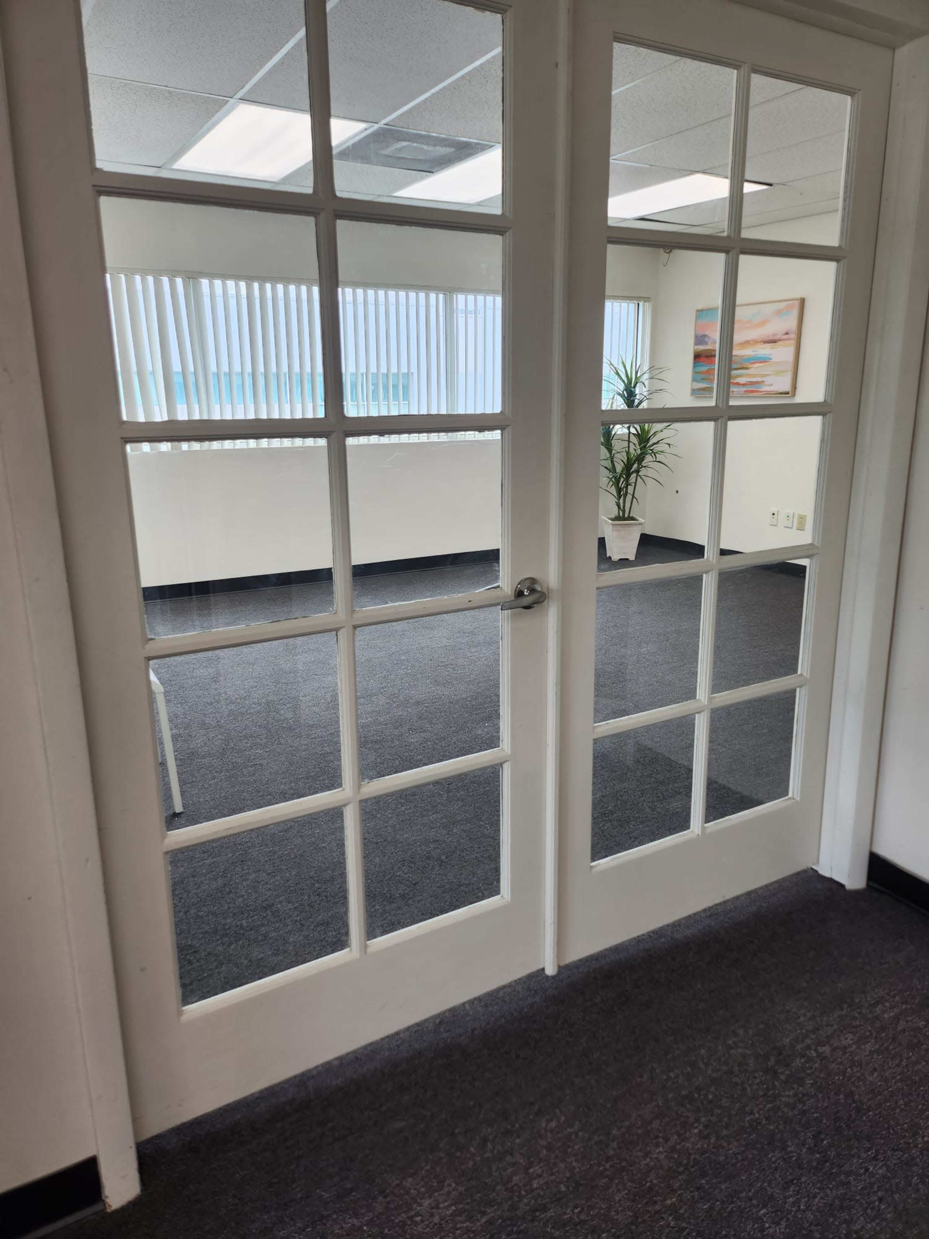 A set of glass-paned double doors leading to a well-lit office space with carpeted flooring and large windows.
