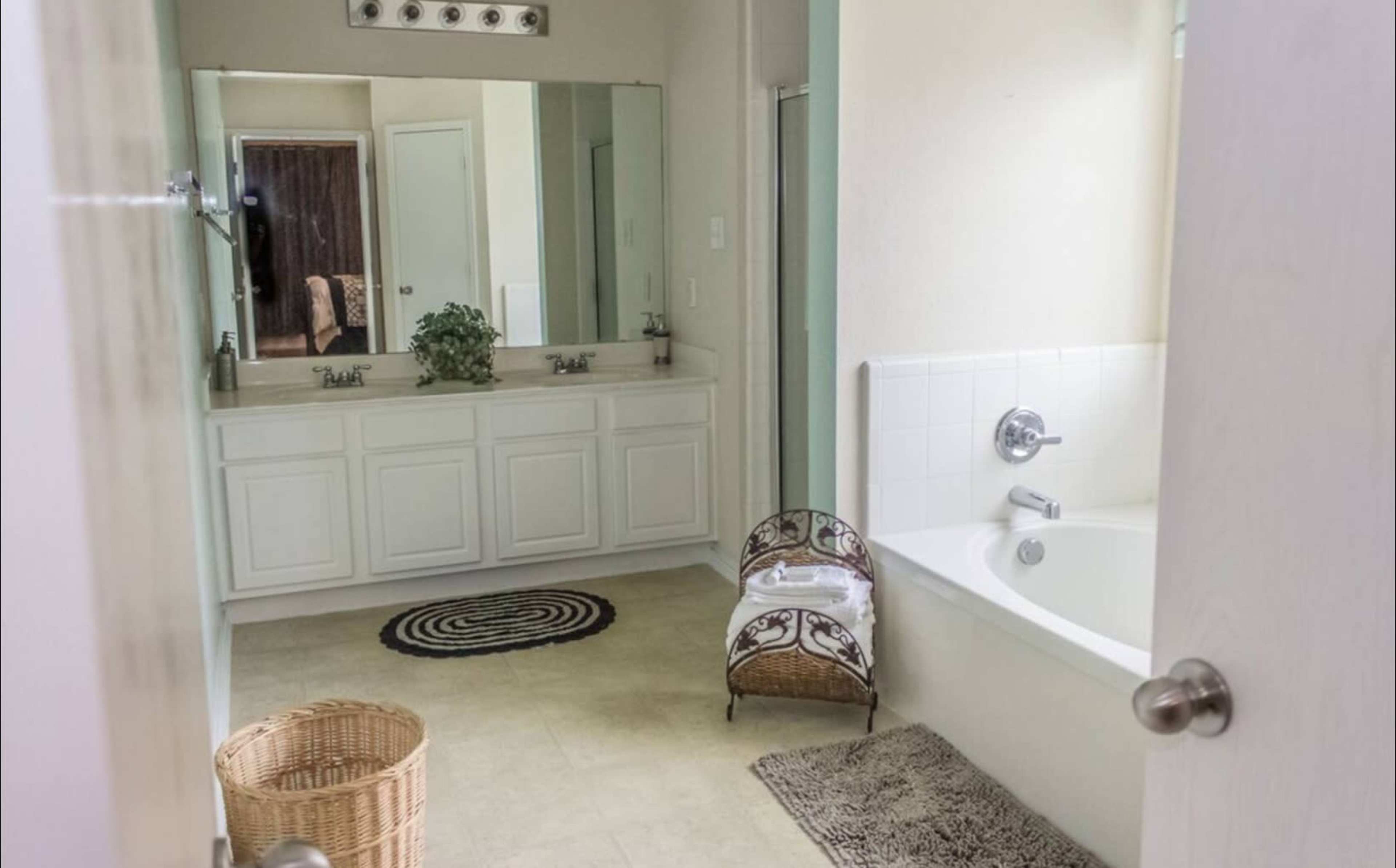A bathroom features a double vanity with mirrors, a bathtub, and a woven basket on the floor.