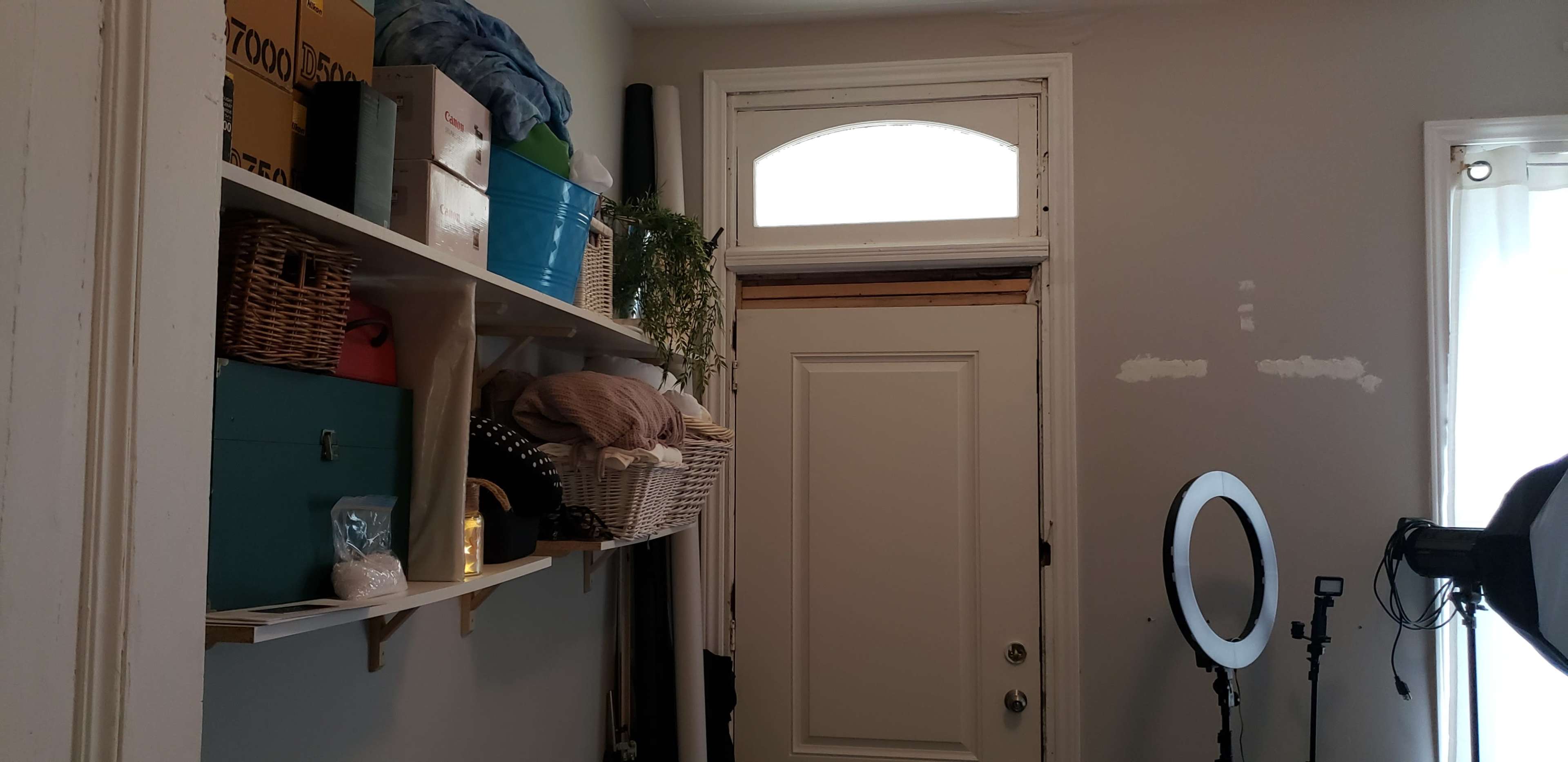 The image shows a small entryway with shelves holding various storage boxes and decorative items, and a door leading outside.