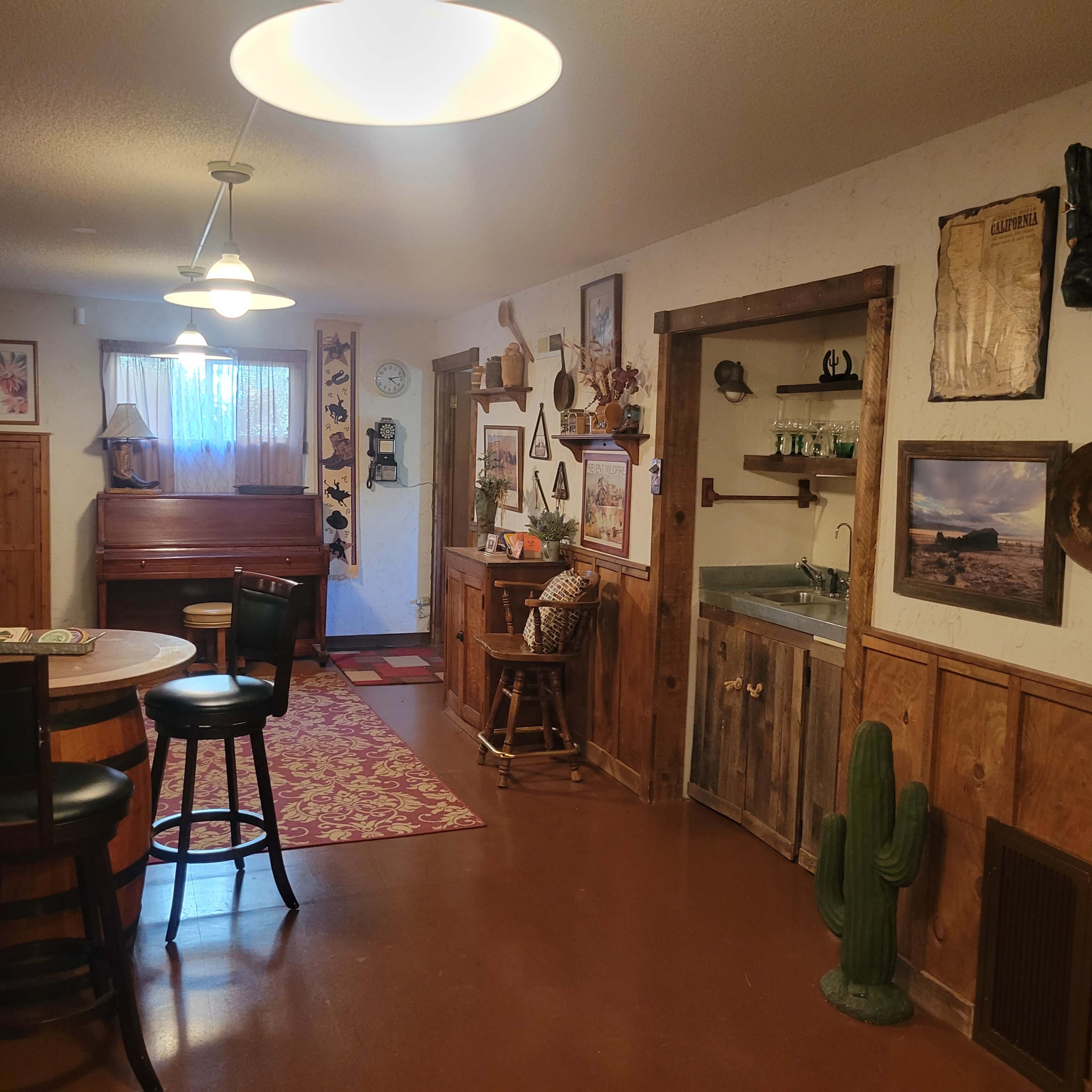 A rustic hallway features a piano, wooden furnishings, and a cactus decoration, with warm light fixtures illuminating the space.