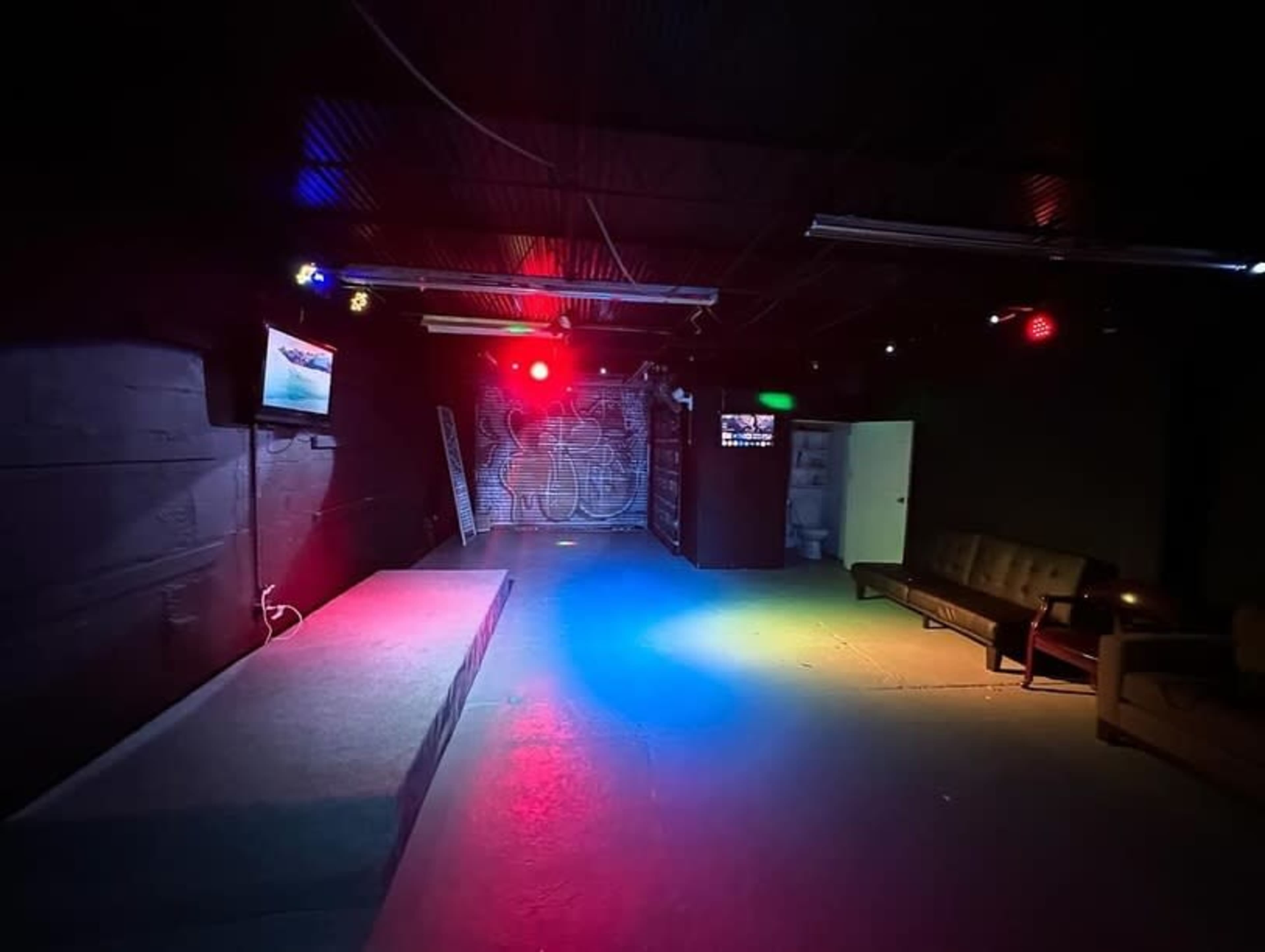 The image shows a dimly lit room with a small stage, a couch, and a TV display on one wall.