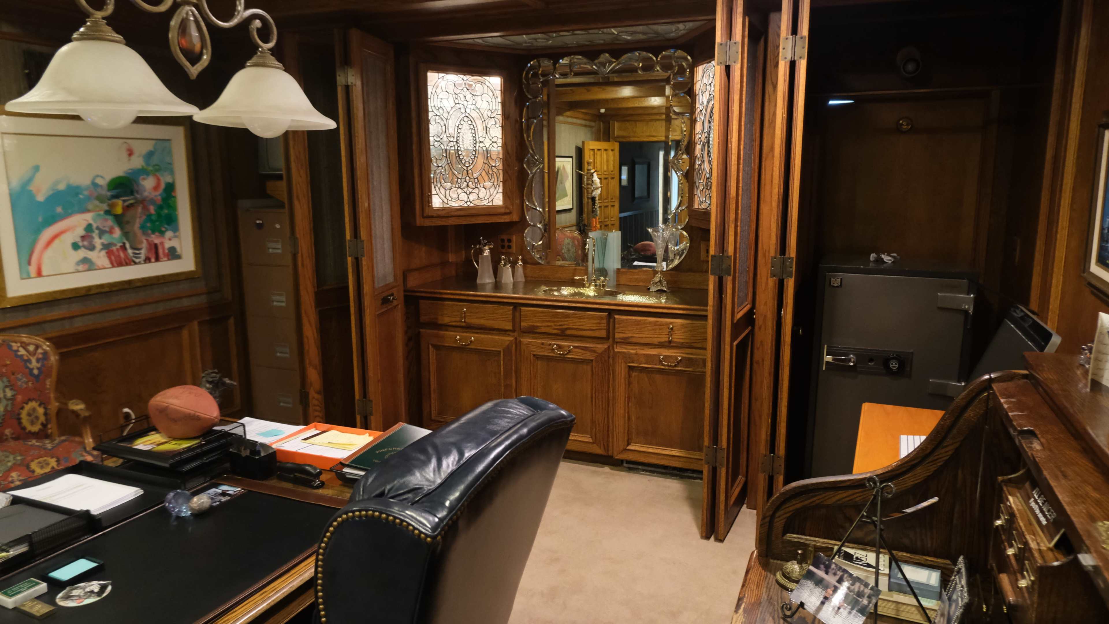 The scene shows a wooden office with a desk, leather chair, and a mirrored cabinet, along with a safe and filing cabinets in the background.