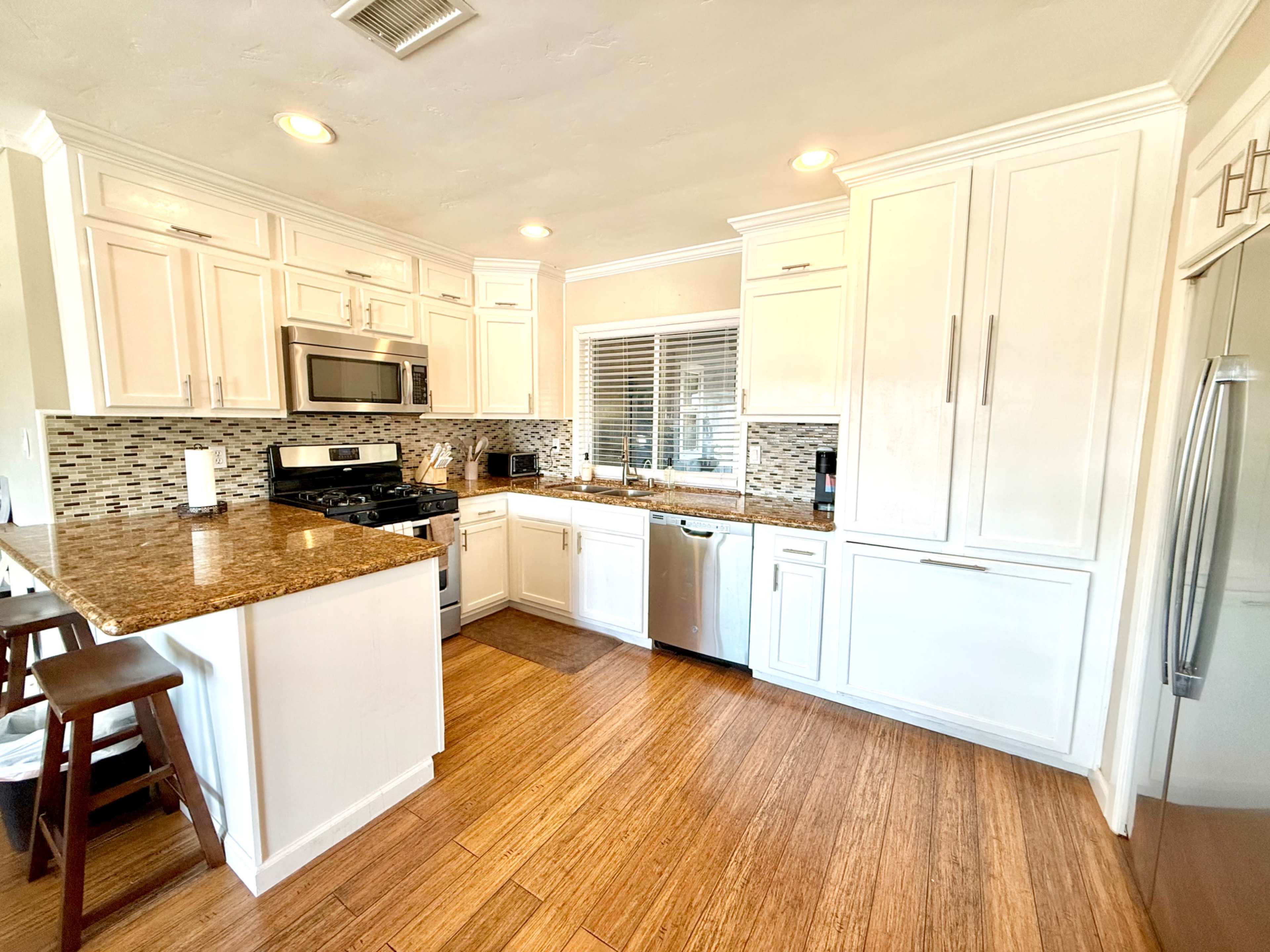 A modern kitchen features white cabinets, stainless steel appliances, a granite countertop, and bamboo flooring.