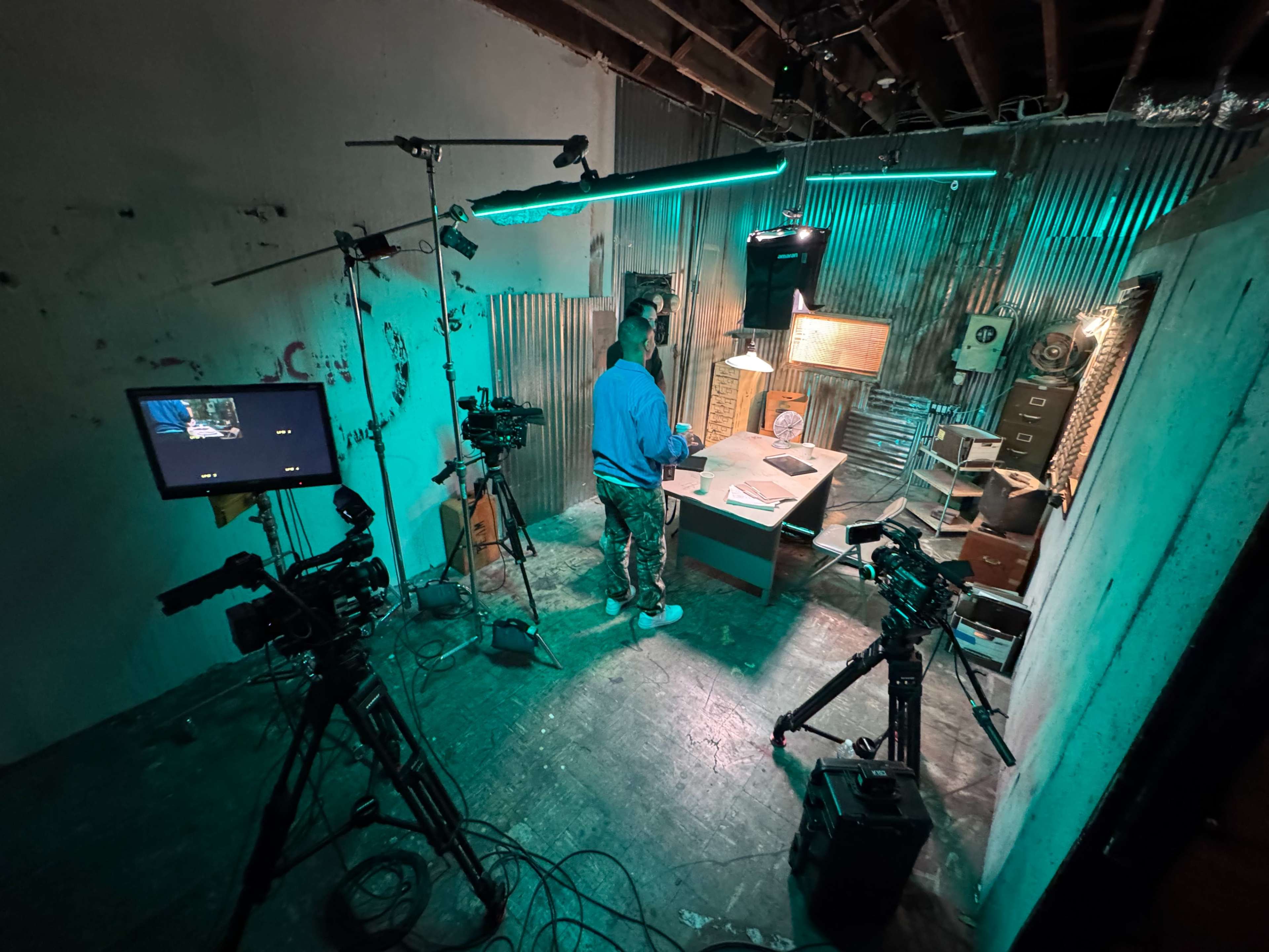 A person stands at a desk surrounded by film equipment in a dimly lit, industrial-style room.