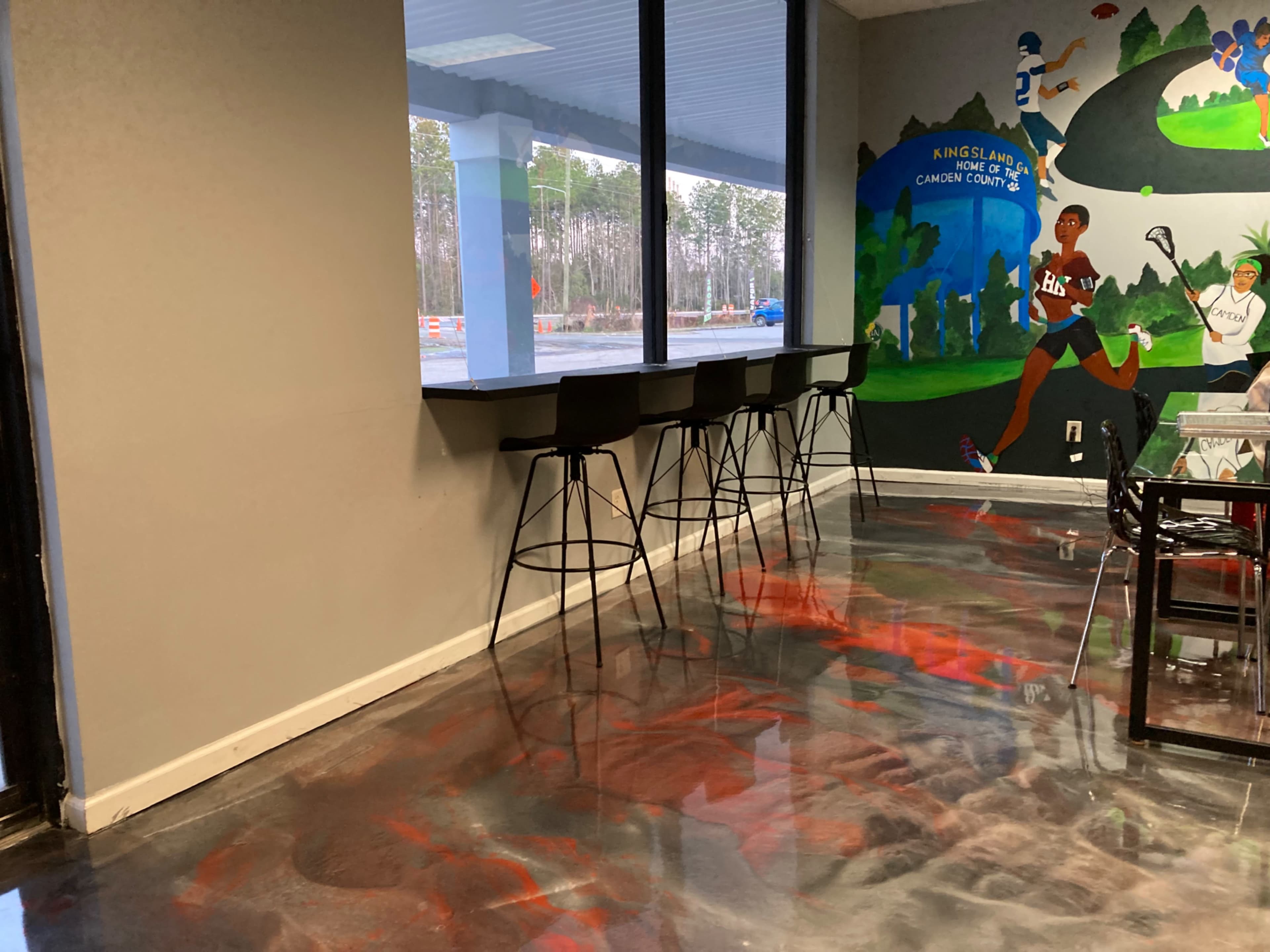 A modern room with a large window, a mural depicting athletic figures, and a polished floor featuring red and black patterns.