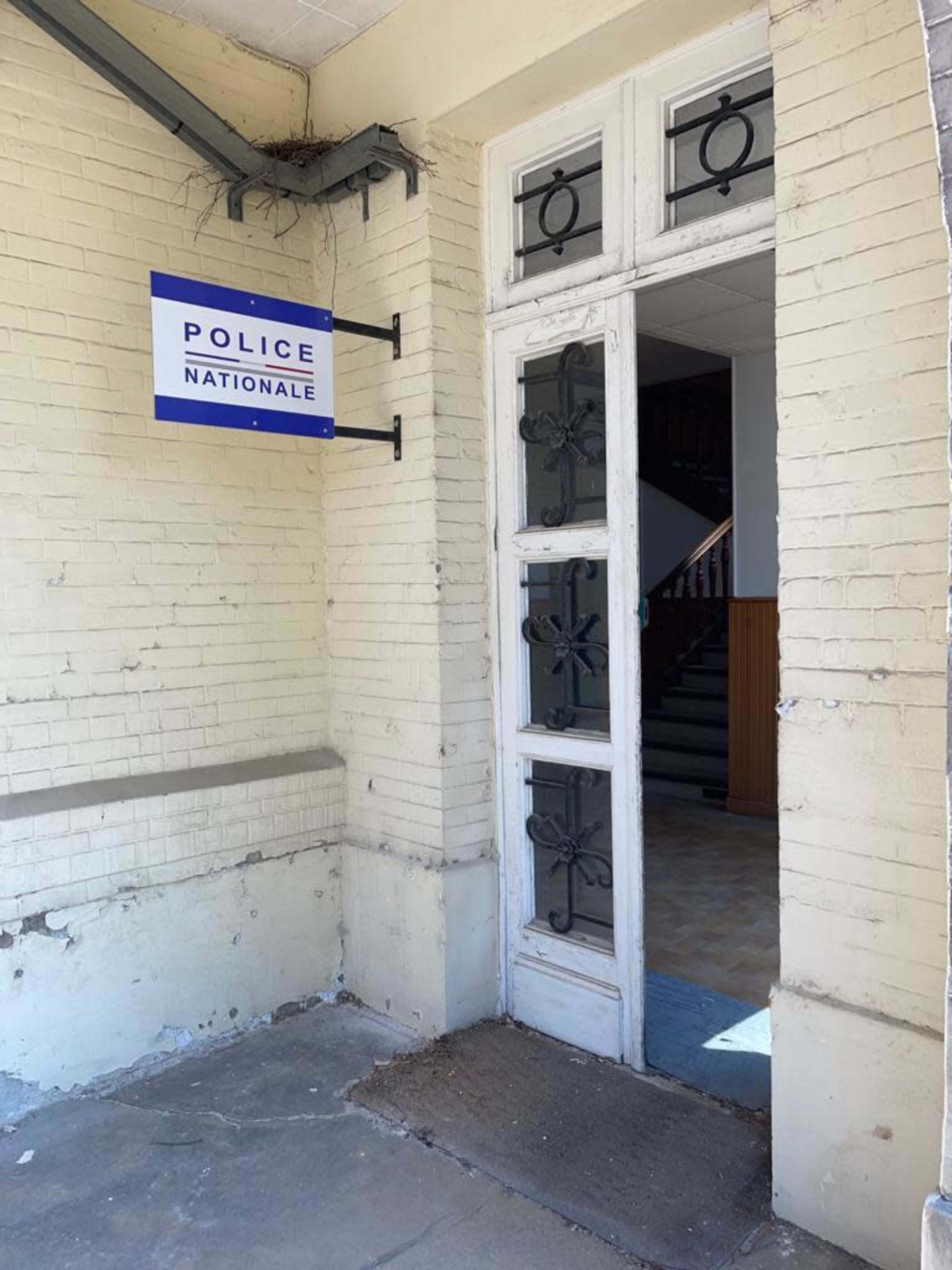 The entrance of a building marked with a "Police Nationale" sign, featuring a set of double doors and a staircase visible in the background.