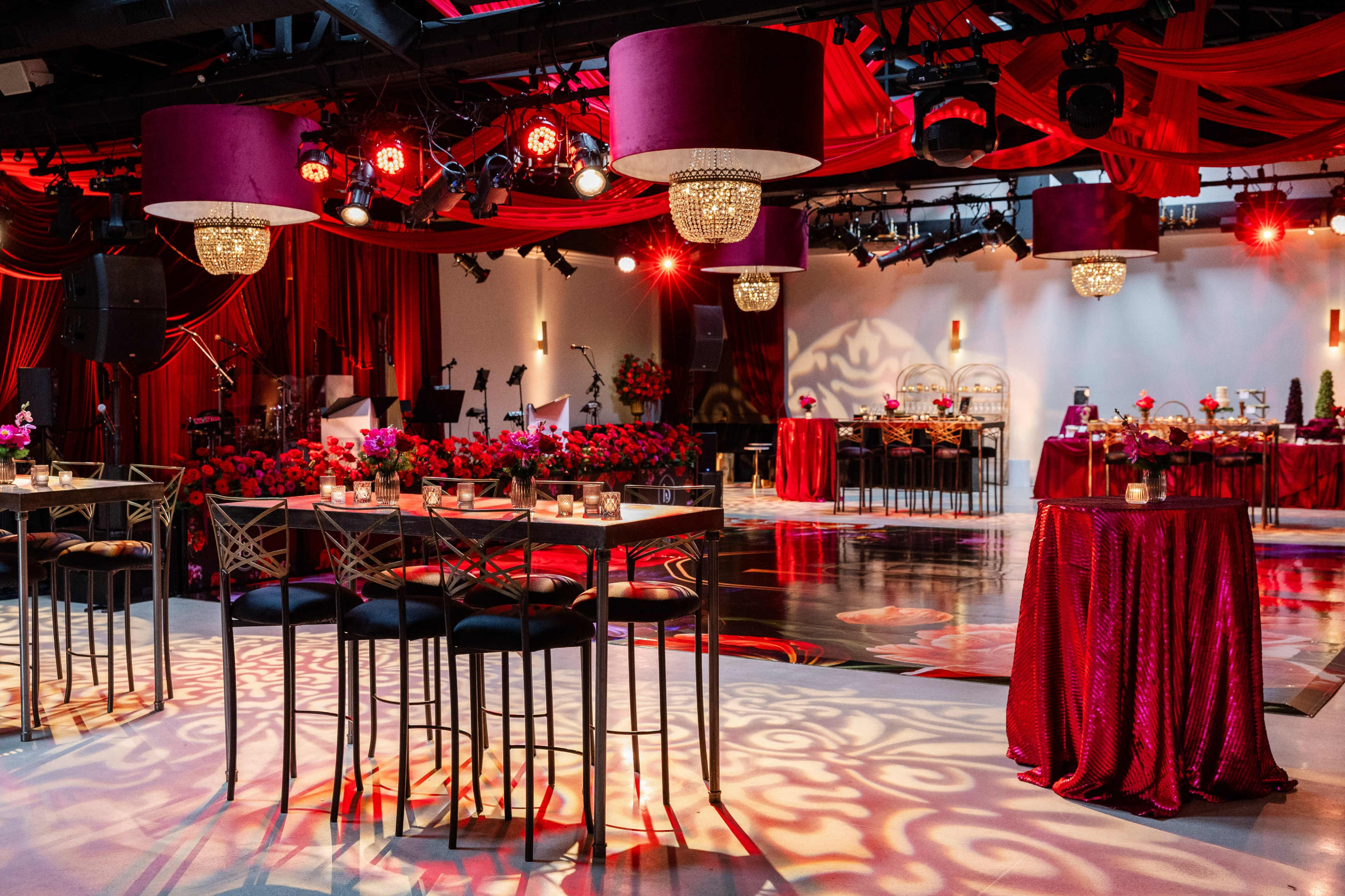 The image shows a glamorous event space decorated with red fabric draping, elegant tables, and centerpieces with floral arrangements.