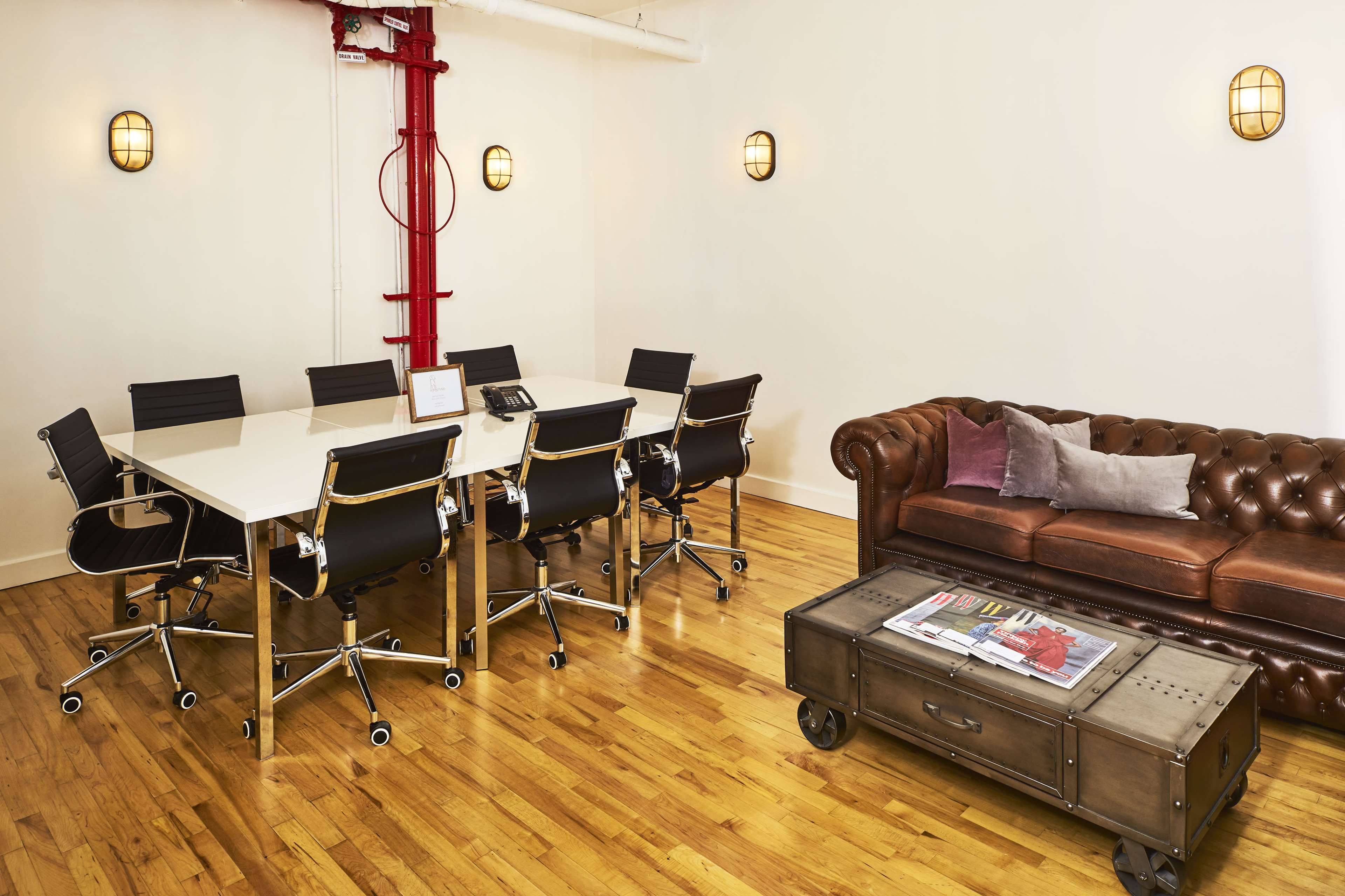 A conference room with a large white table surrounded by black chairs, a brown leather couch, and a coffee table on a hardwood floor.