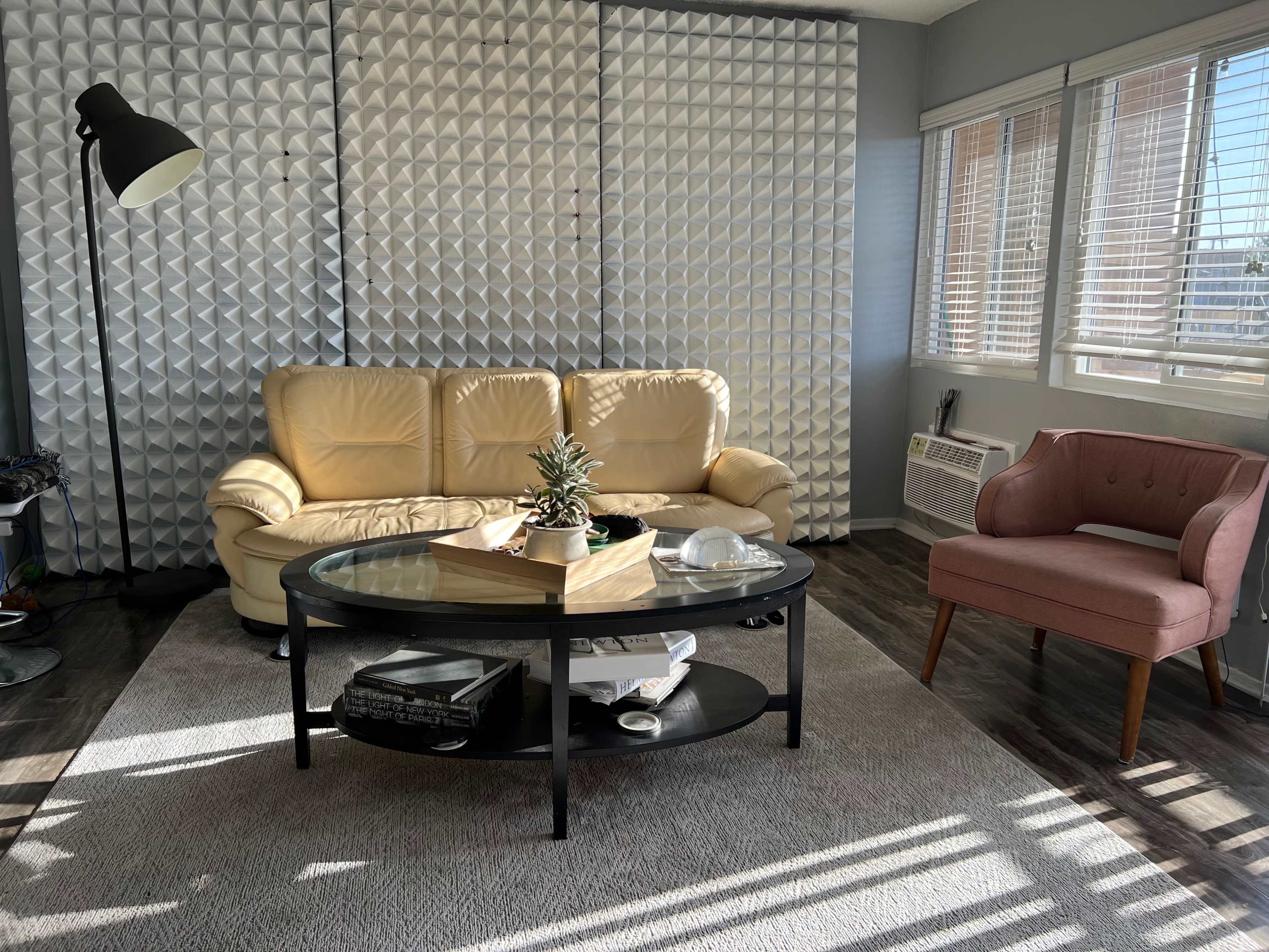 A living room with a beige leather sofa, a pink chair, a round glass coffee table, and a textured wall in the background.