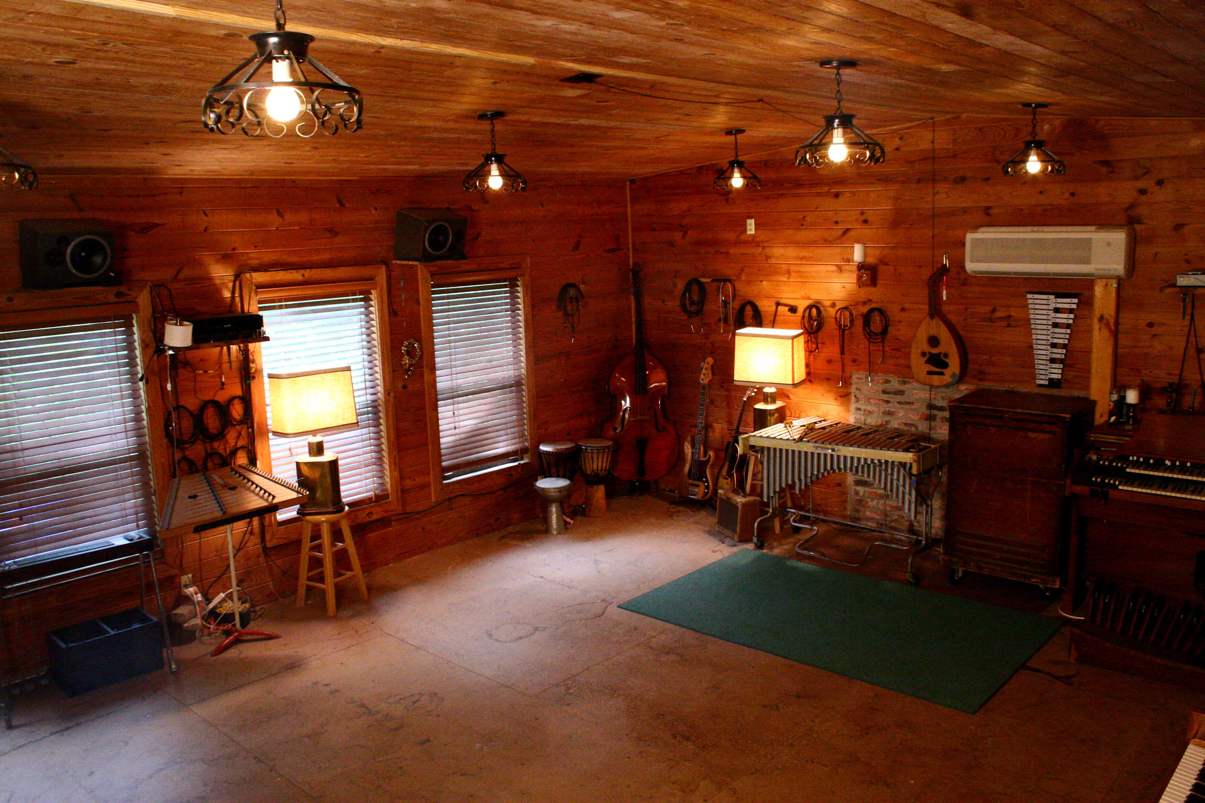 A wooden room with musical instruments, including a guitar, a xylophone, and various other instruments, illuminated by overhead lights.