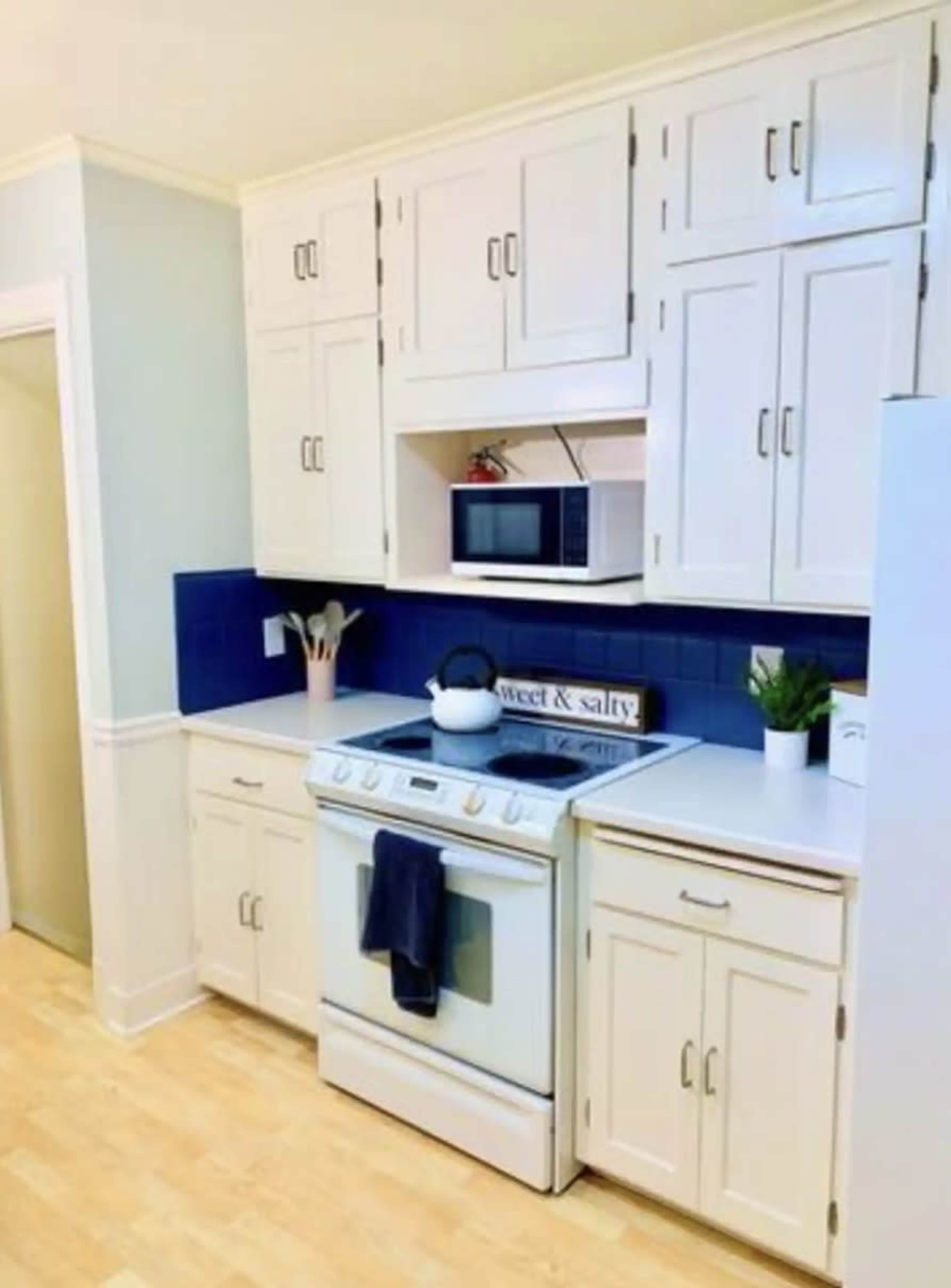 A modern kitchen with white cabinetry, a blue backsplash, a microwave above an oven, and a small plant on the countertop.