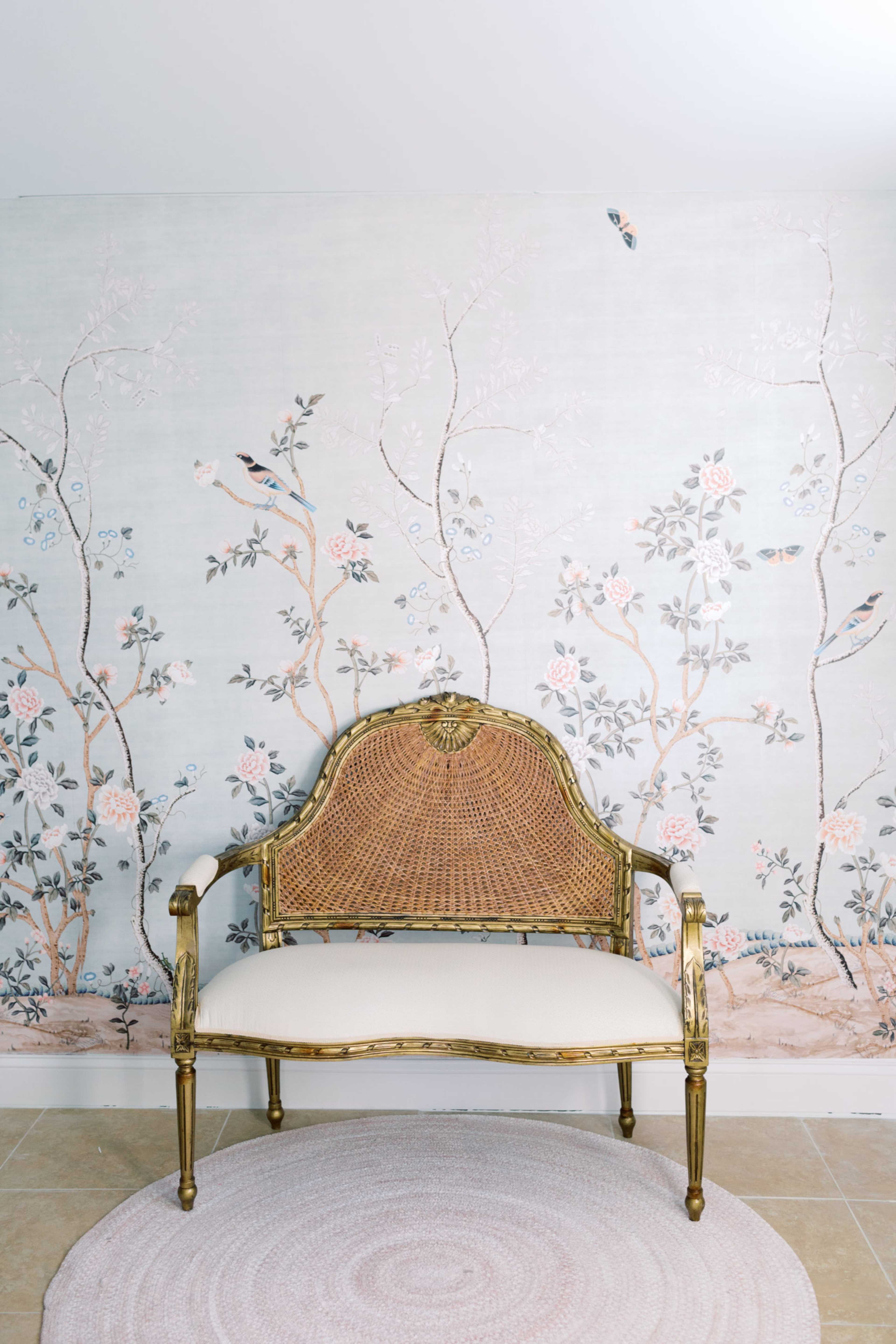 A gold-framed, upholstered settee is positioned against a floral wallpaper featuring birds and branches.