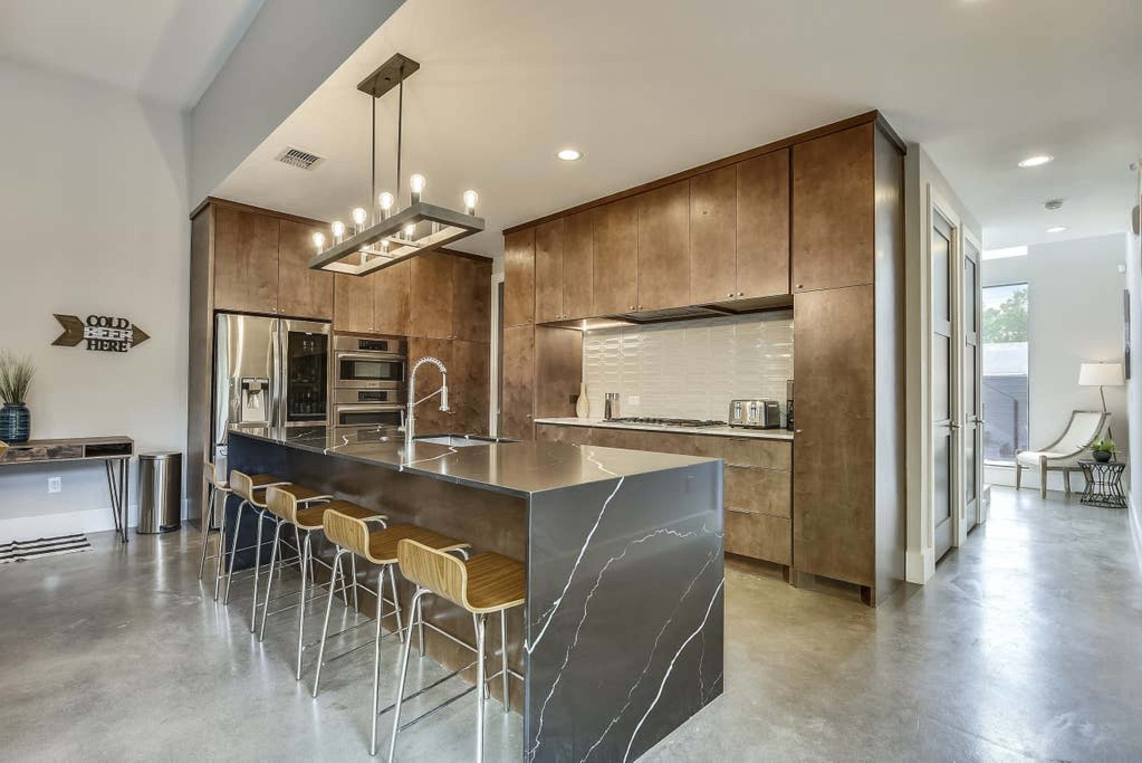 A modern kitchen features a central island with bar seating, stainless steel appliances, and brown cabinetry.
