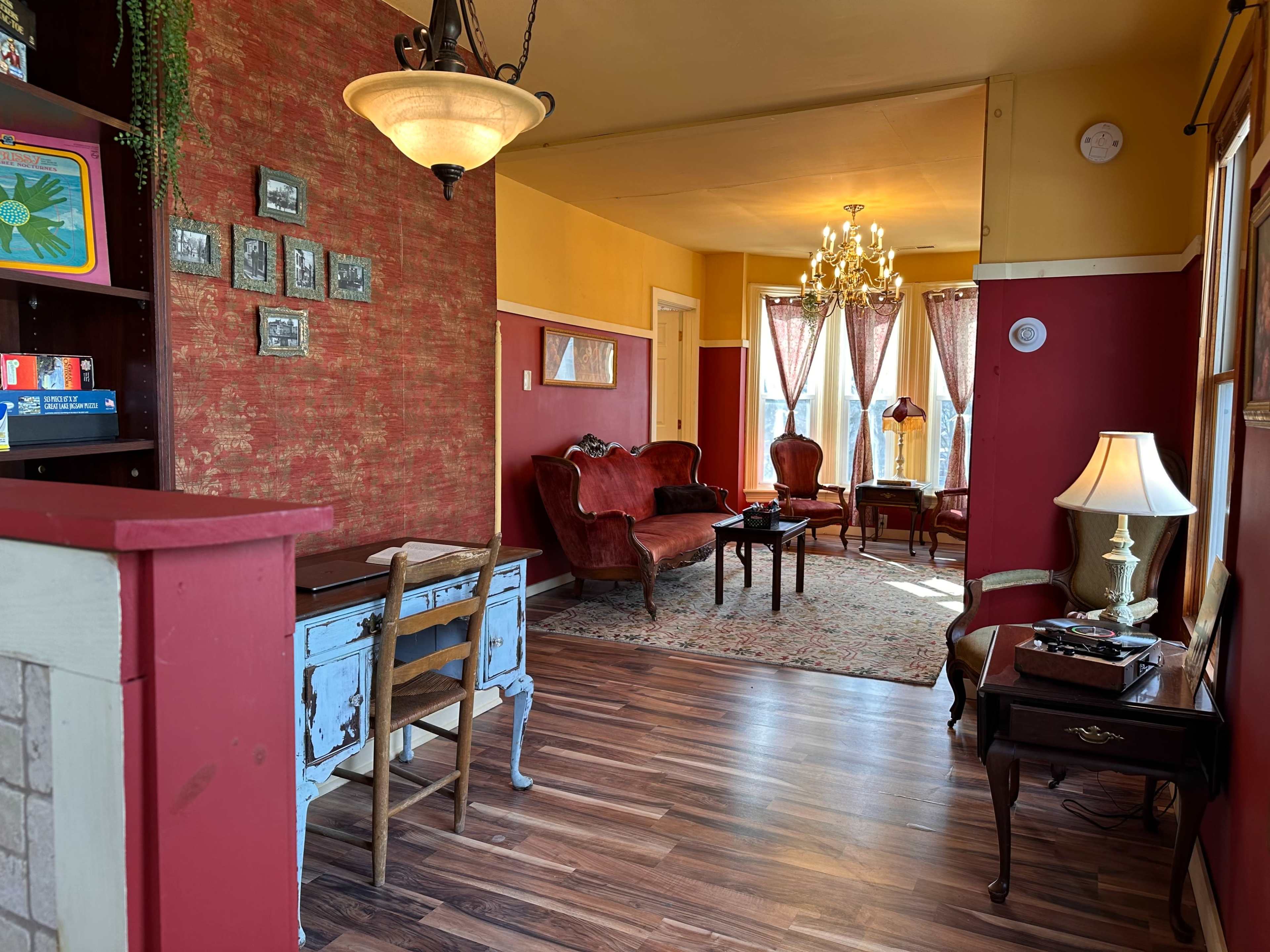The image shows a cozy living space with a mix of red and yellow walls, vintage furniture, and a chandelier hanging from the ceiling.