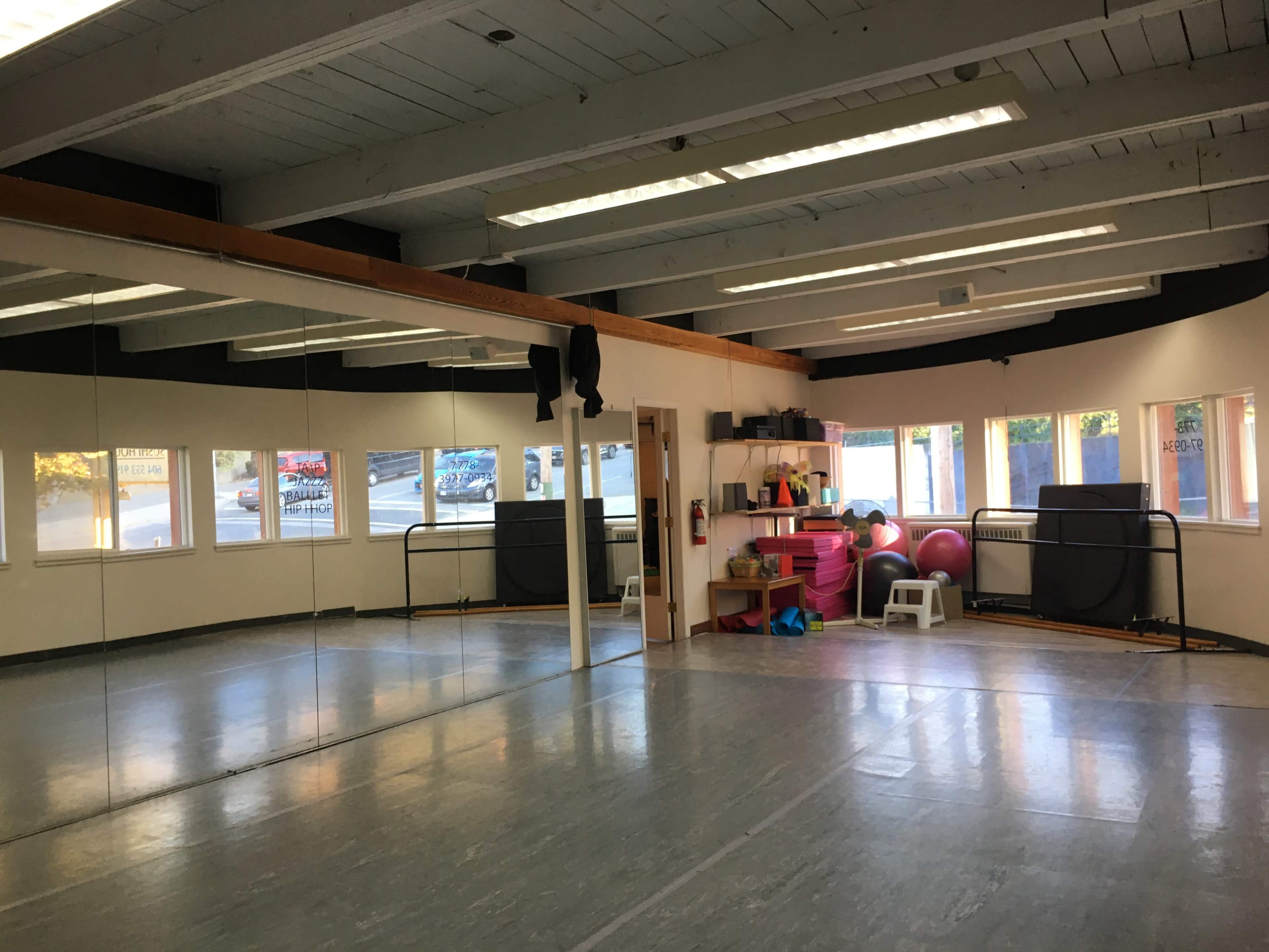 A spacious exercise studio with large mirrors, fitness equipment, and windows allowing natural light.