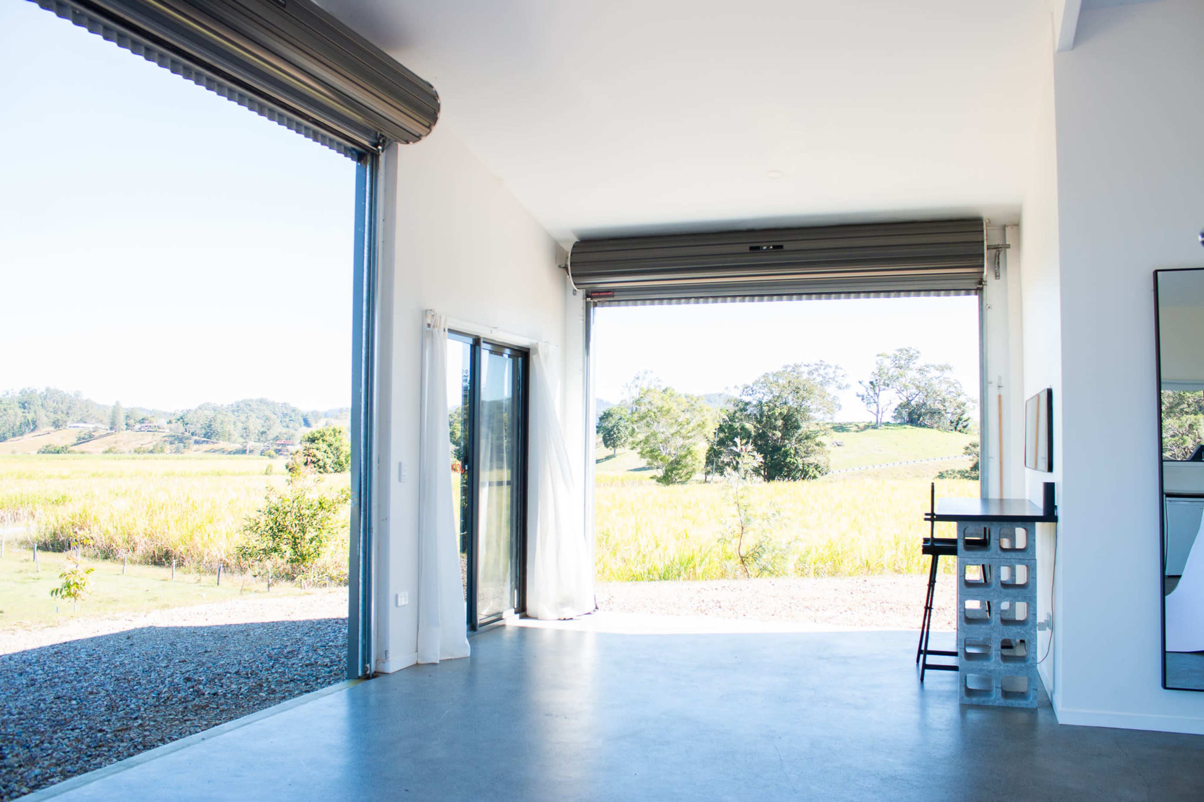 The image shows an interior space with large open doors leading to a scenic vineyard landscape.