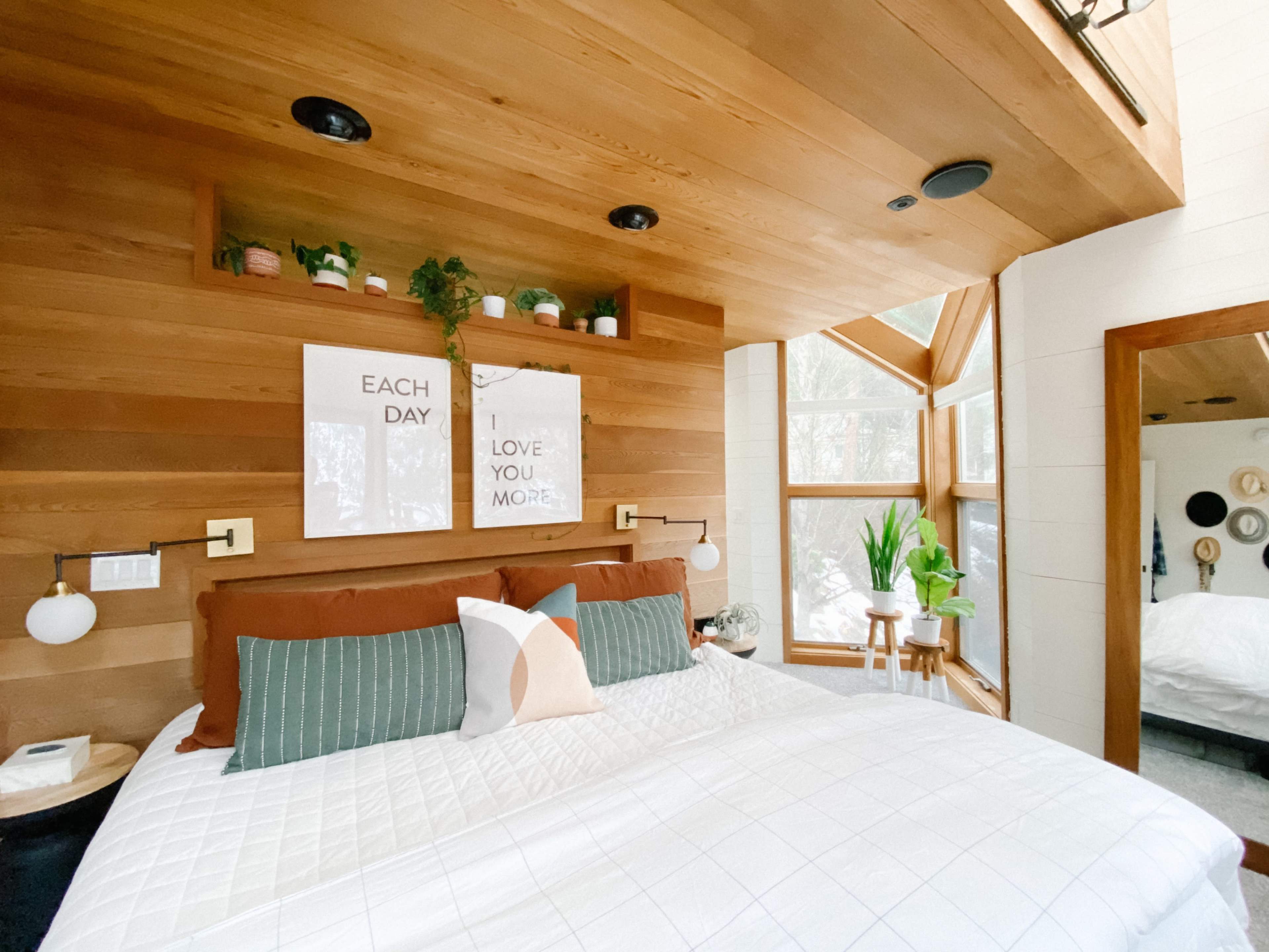 A cozy bedroom featuring a wooden accent wall, a large bed with white bedding, and framed wall art above the bed.