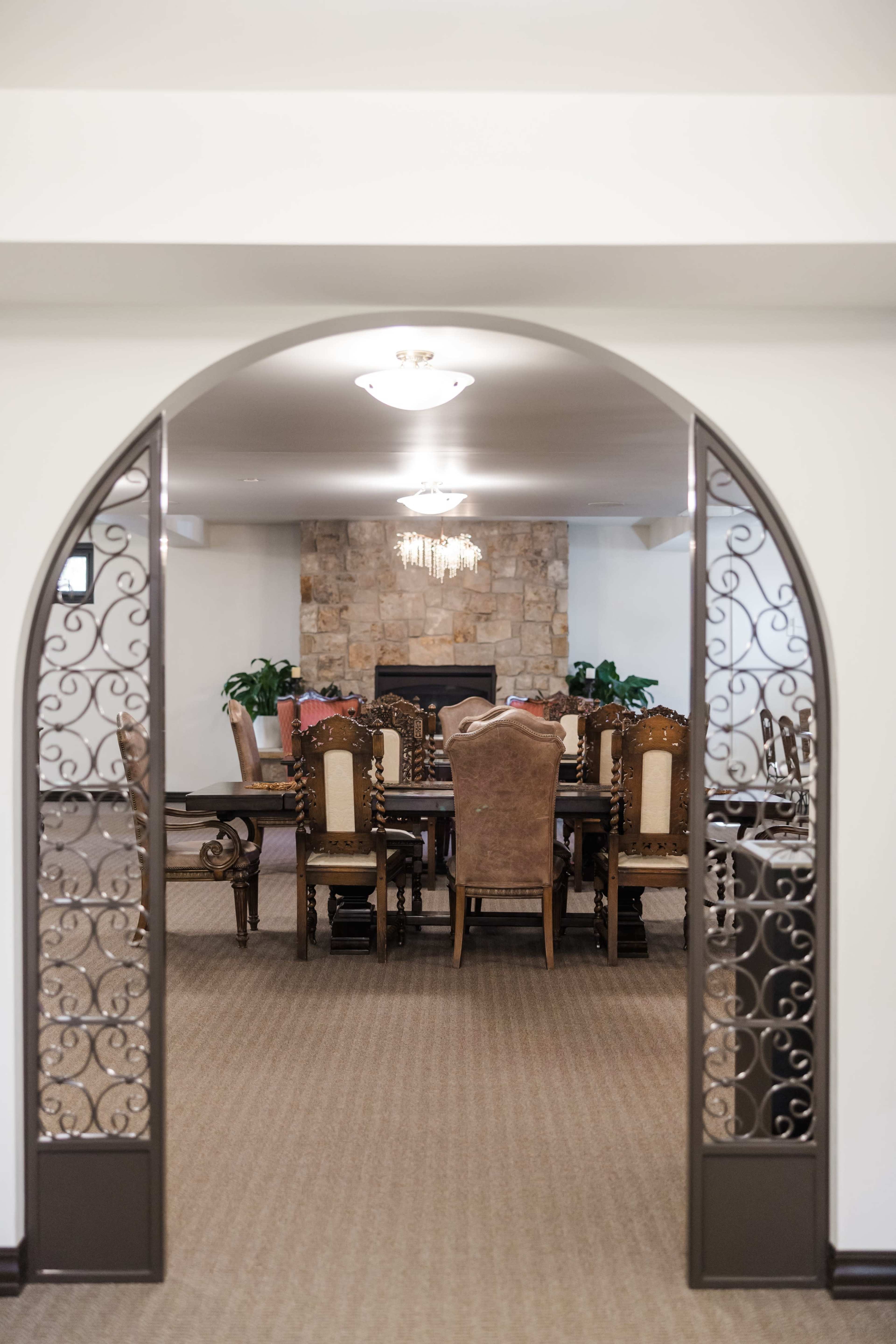 A dining room with a large wooden table and upholstered chairs is visible through an arched entrance adorned with decorative metalwork.
