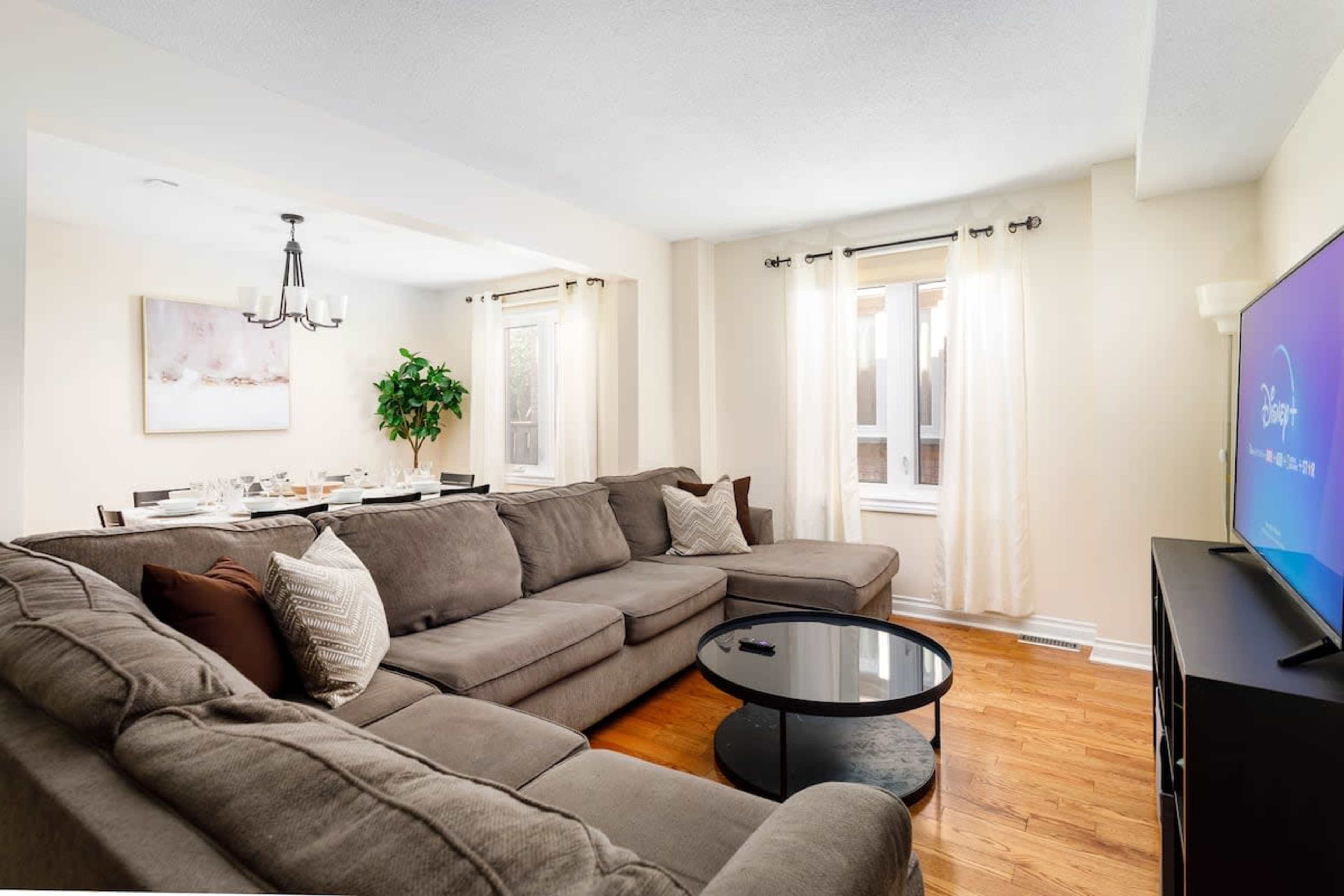 A spacious living room features a large sectional sofa, a glass coffee table, and a dining area with a table set for six.