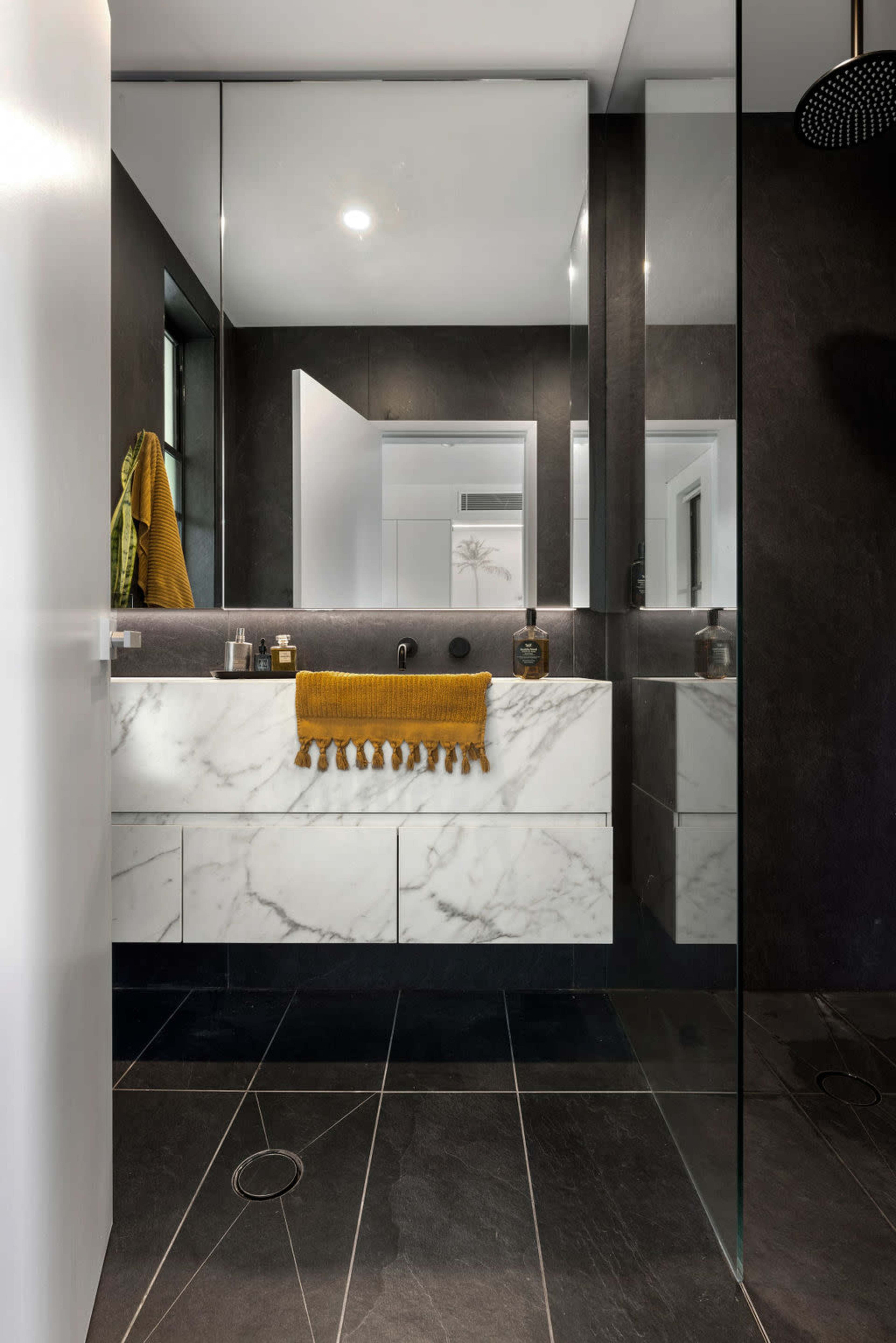 A modern bathroom featuring a marble vanity with storage drawers, dark tiled flooring, and large mirrors reflecting the space.