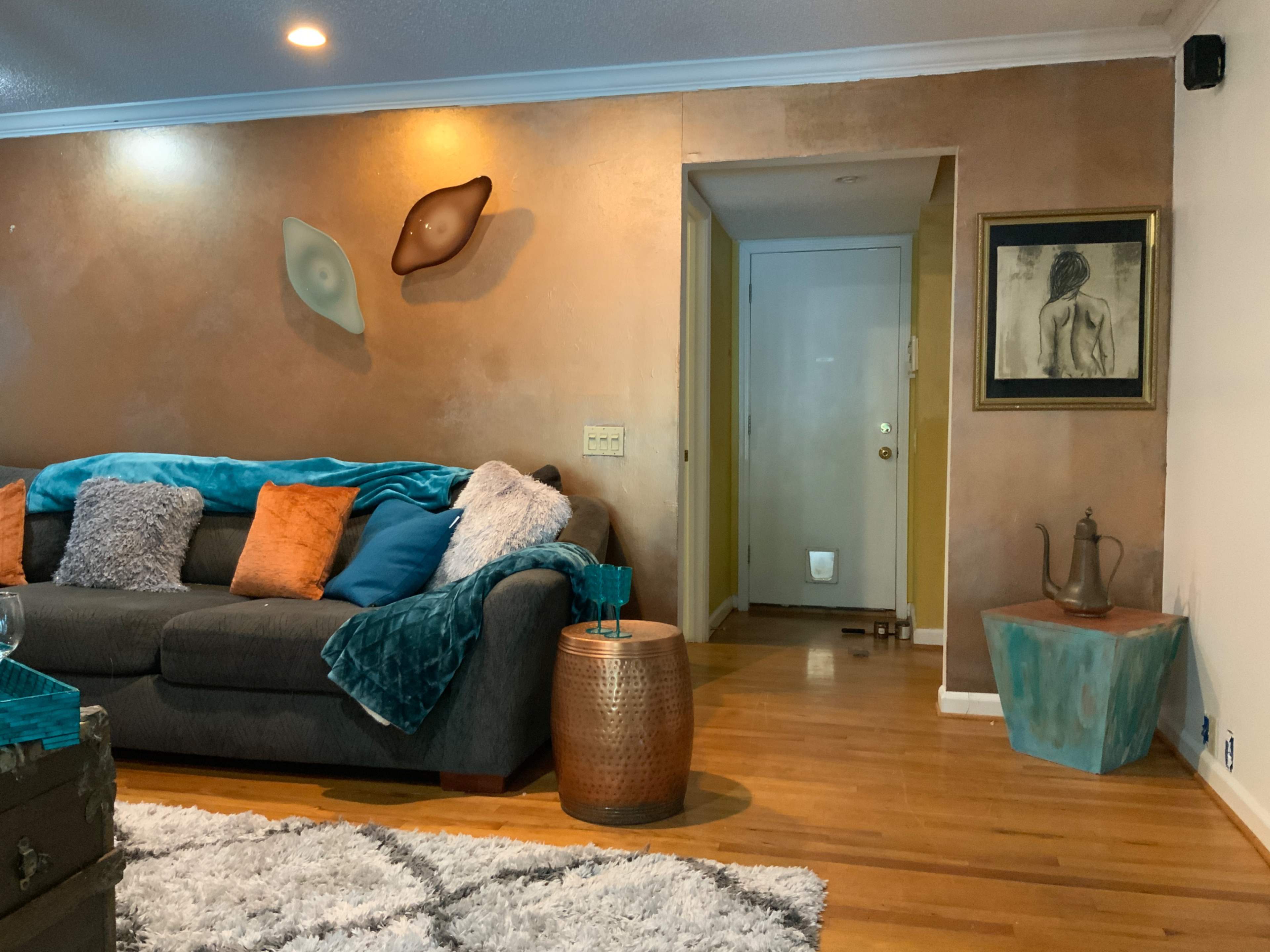 The living room features a gray couch adorned with colorful pillows, a textured area rug, and artwork on the walls.