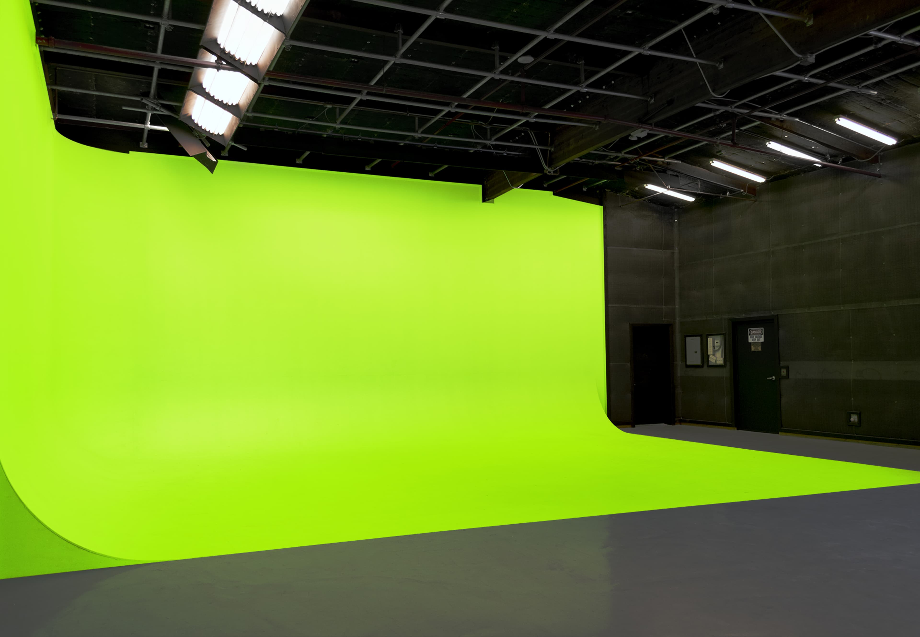 A spacious studio with a bright green screen background and gray flooring.