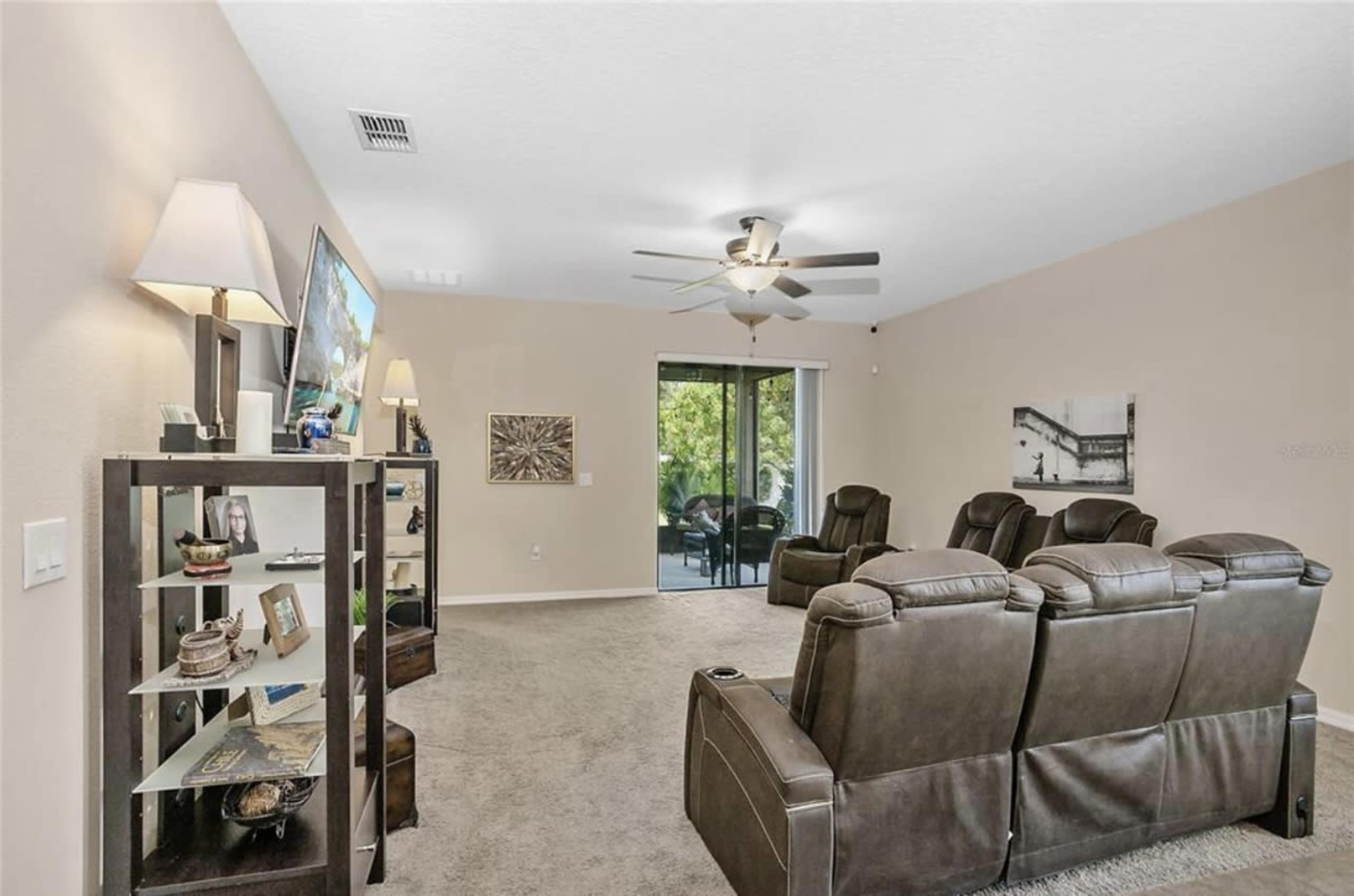 A spacious living room with recliner chairs, a ceiling fan, and a large sliding glass door leading to an outdoor area.