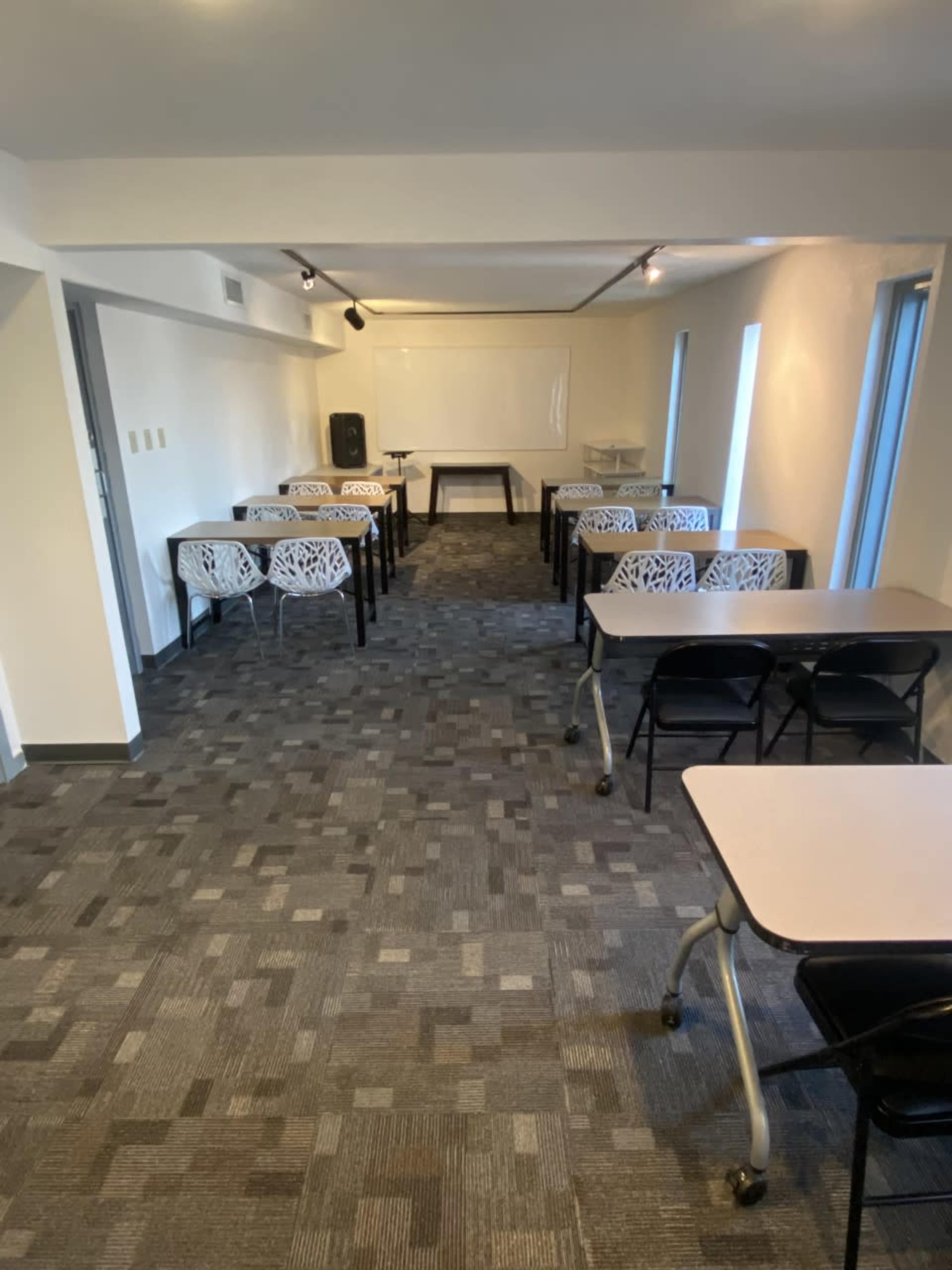 The image shows a classroom or meeting room with several tables arranged neatly in rows on a carpeted floor.