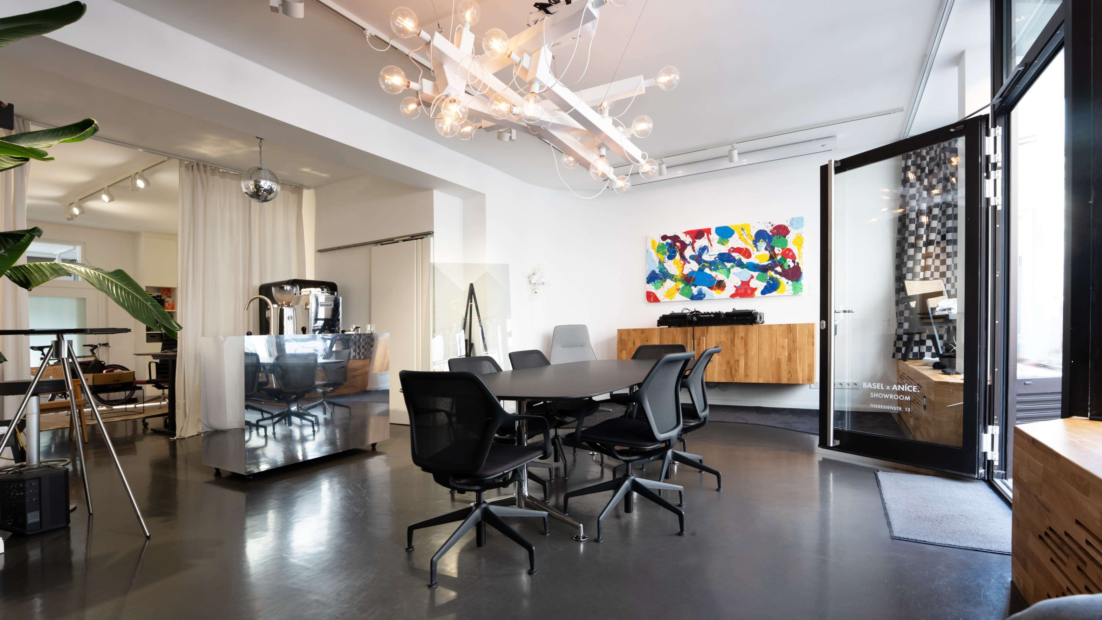 The image shows a modern office space featuring a large conference table surrounded by black chairs, a colorful artwork on the wall, and sleek furniture.