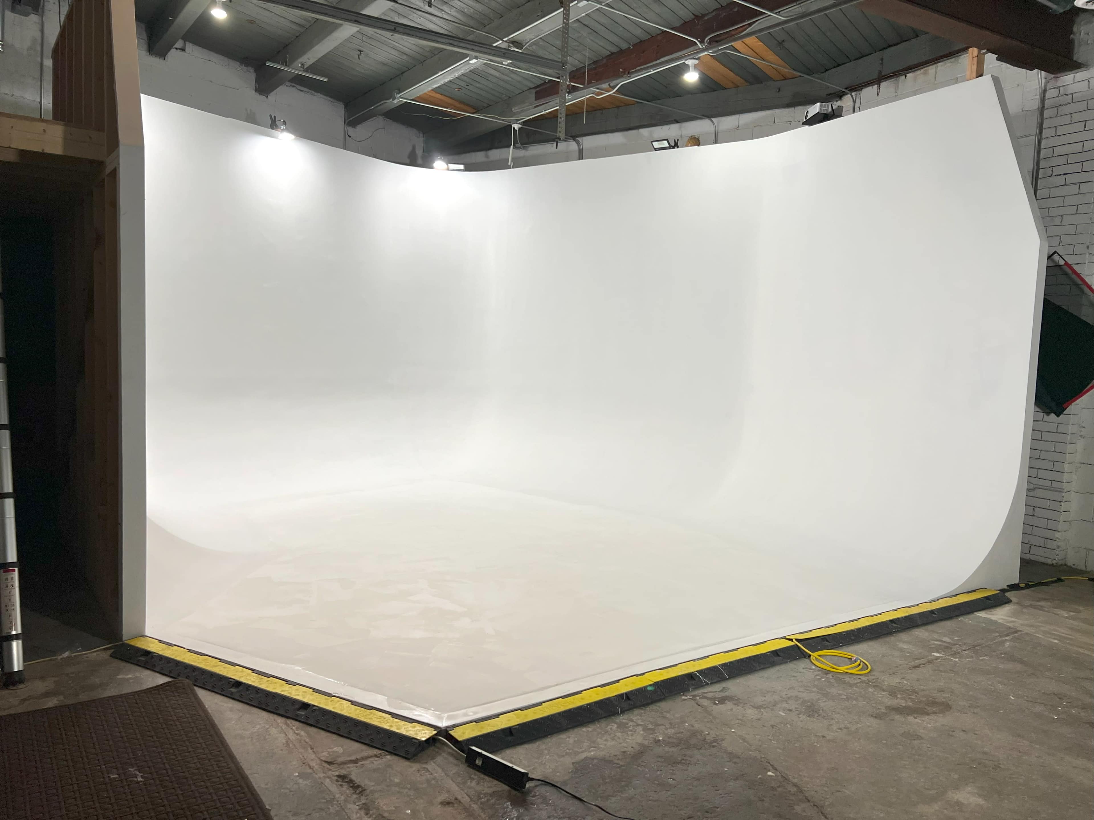 A large, blank white photography studio with a seamless backdrop and concrete floor.
