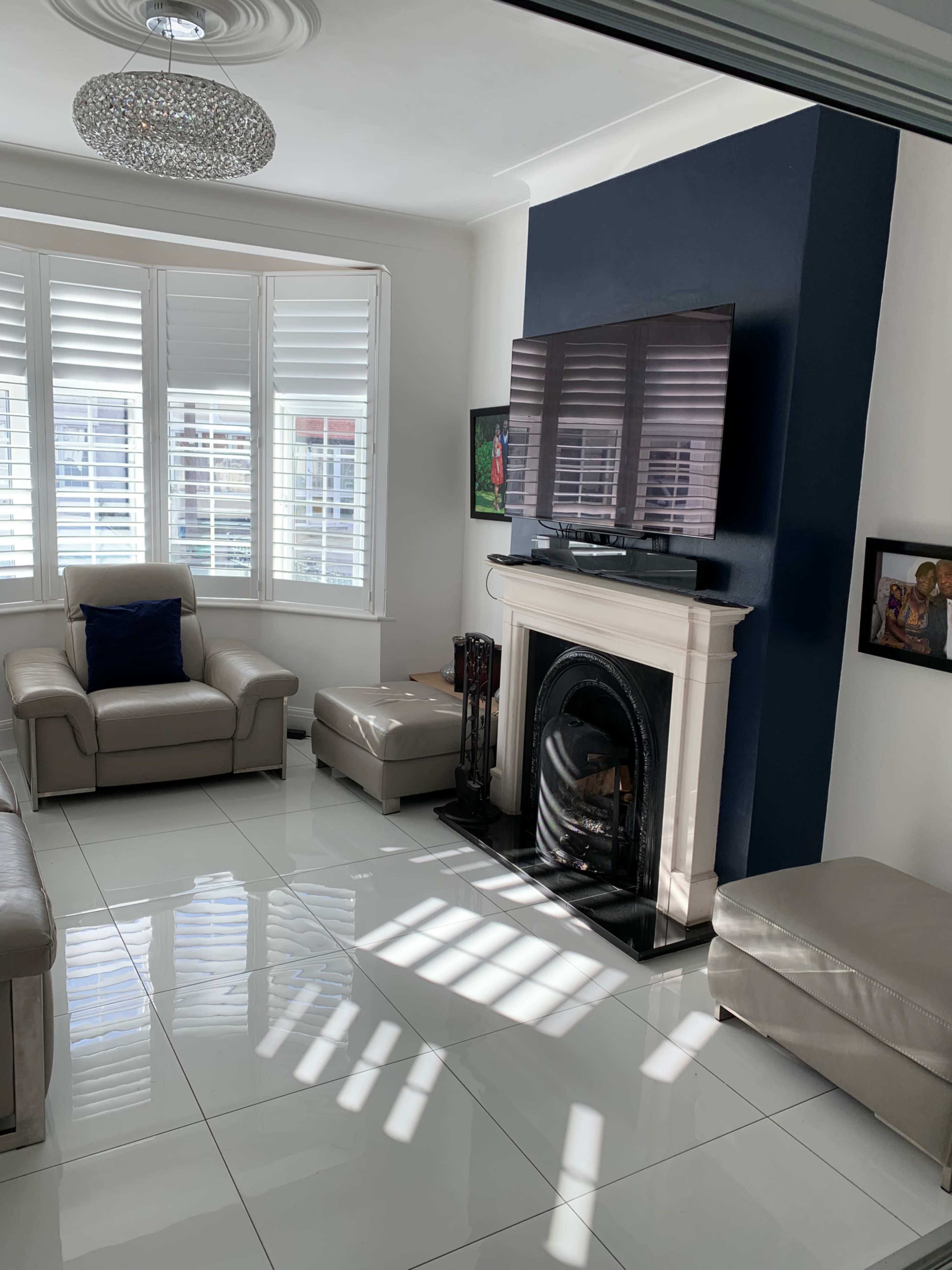 The image shows a modern living room with a television mounted on a dark blue wall, a fireplace, and a shiny white tiled floor.