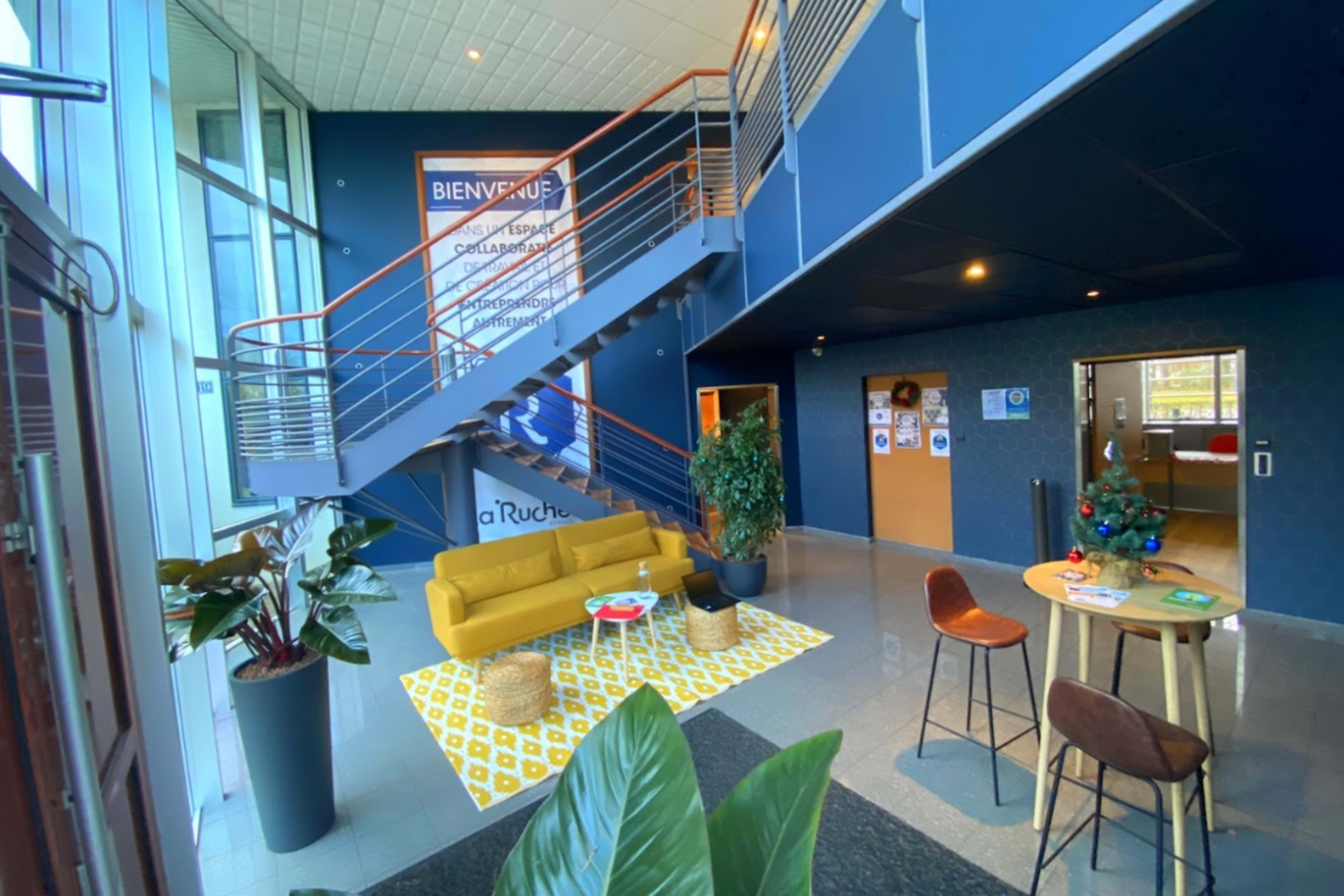 A modern lobby area with a yellow sofa, a coffee table, and a staircase leading to an upper level.