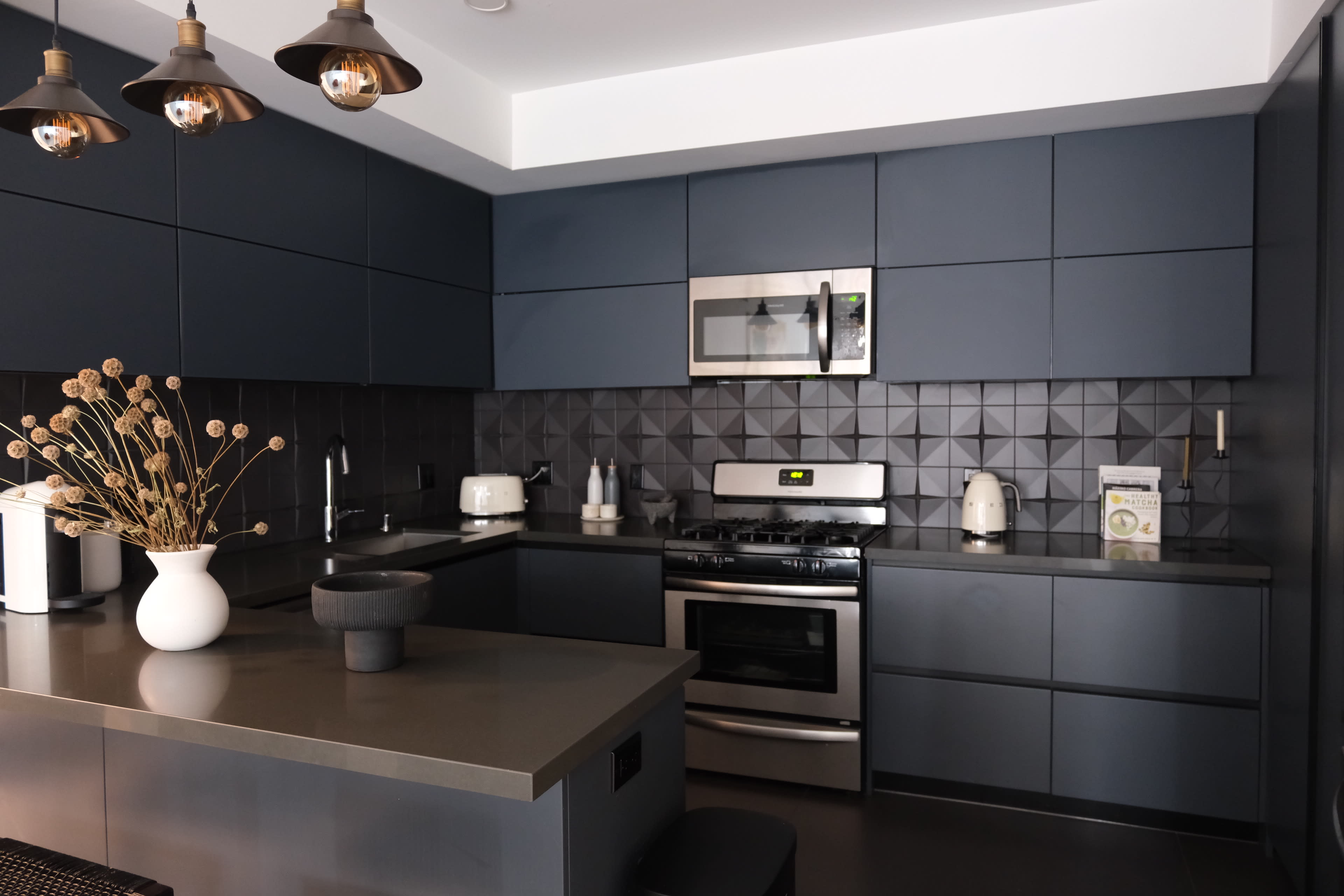 The image shows a modern kitchen featuring dark blue cabinetry, stainless steel appliances, and a gray countertop.